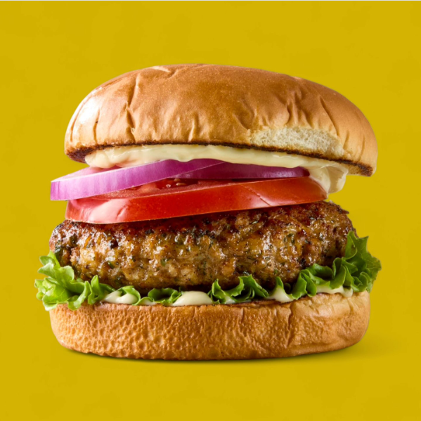Close-up of a hamburger with lettuce, a beef patty, tomato, onions, mayonnaise, all inside a toasted bun against a yellow background.
