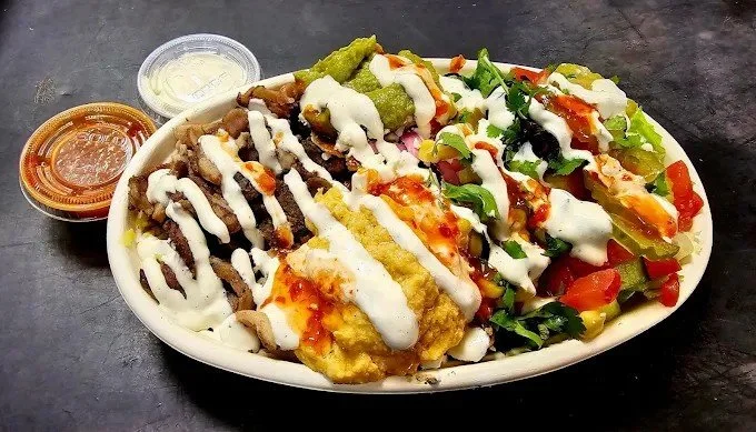 A white oval dish containing nachos topped with cheese, sour cream, jalapenos, and salsa. Two small containers of salsa and sour cream are placed beside the dish.
