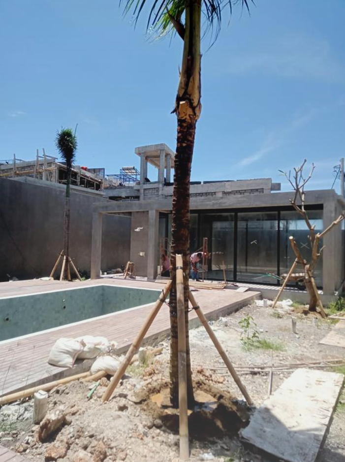 Construction site of a modern house with a pool, palm trees, and workers, under a clear blue sky.