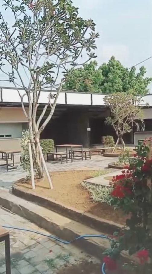 An outdoor patio area with trees, plants, benches, and a building in the background.