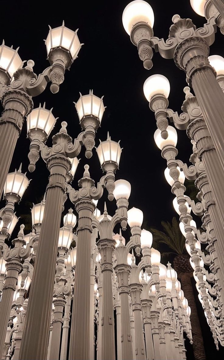 Outdoor art installation of numerous vintage-style street lamps with white globes arranged closely together against a dark night sky.