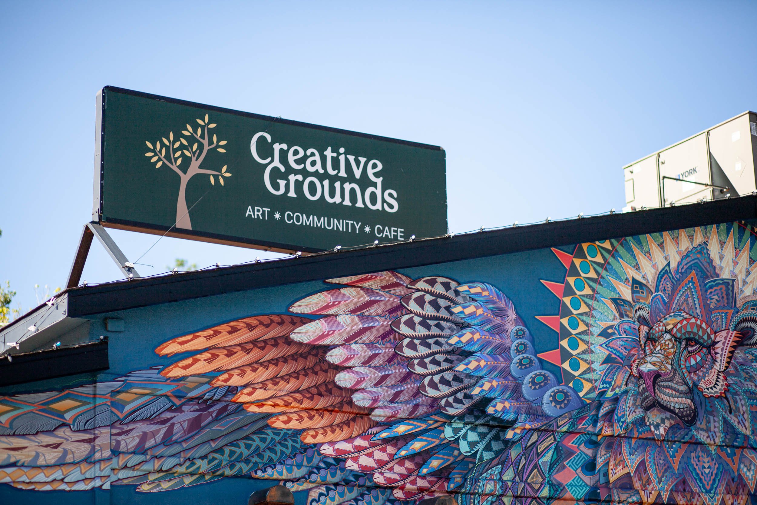 Colorful umbrellas arranged in a layered display beneath a sign for Creative Grounds, which offers art, community, and cafe.