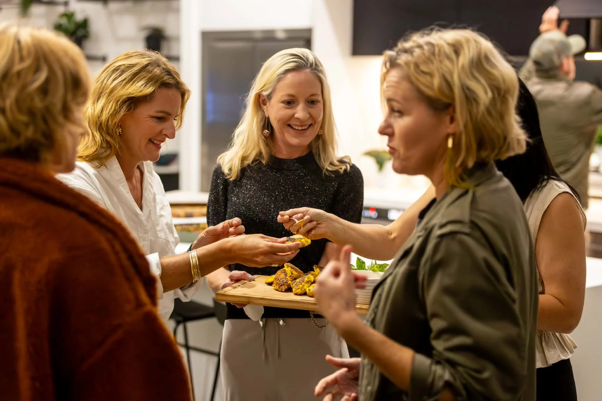 Women socializing at a gathering while sharing food on a wooden serving board