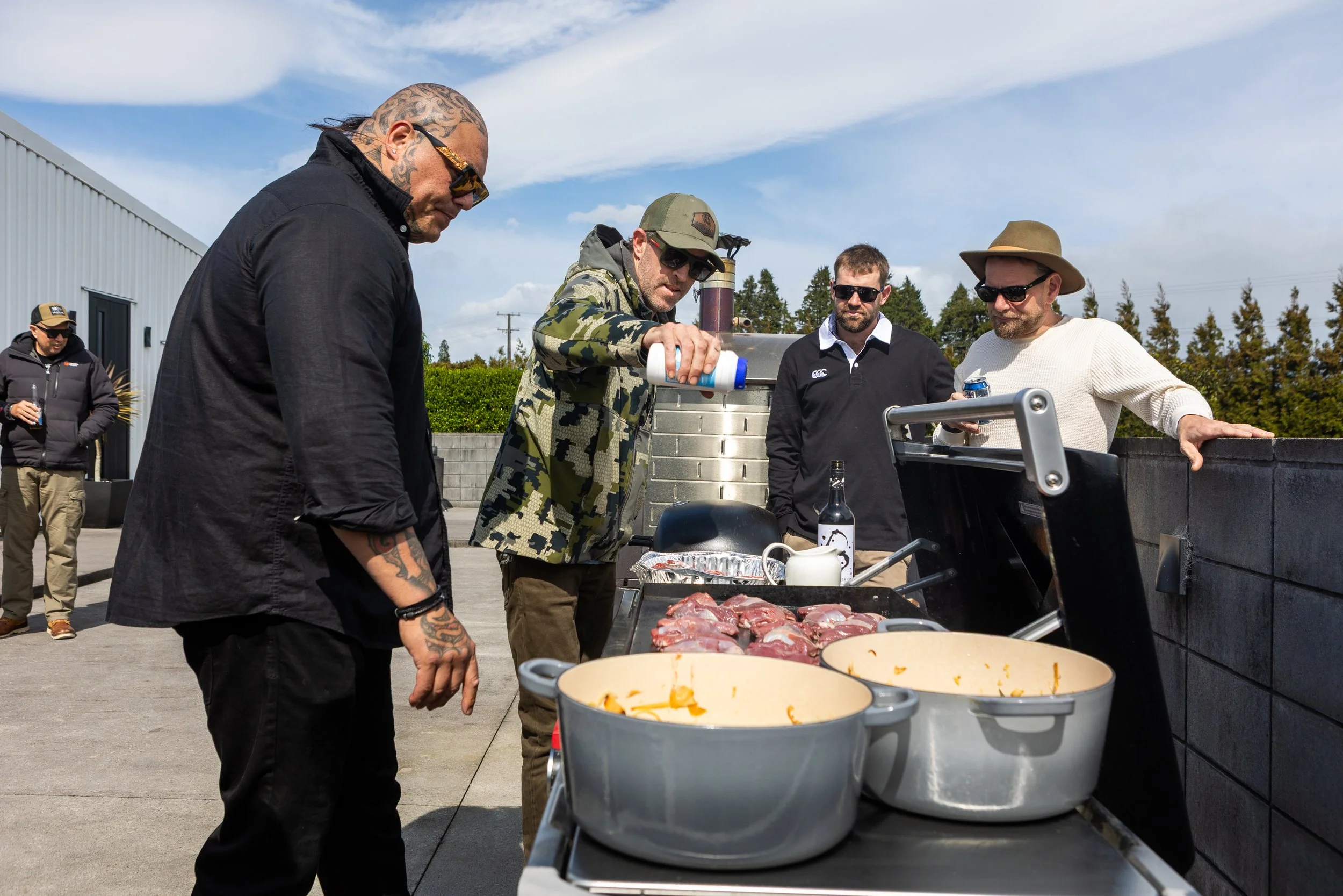 Group of men cooking meat outdoors on a large grill with pots and cooking equipment