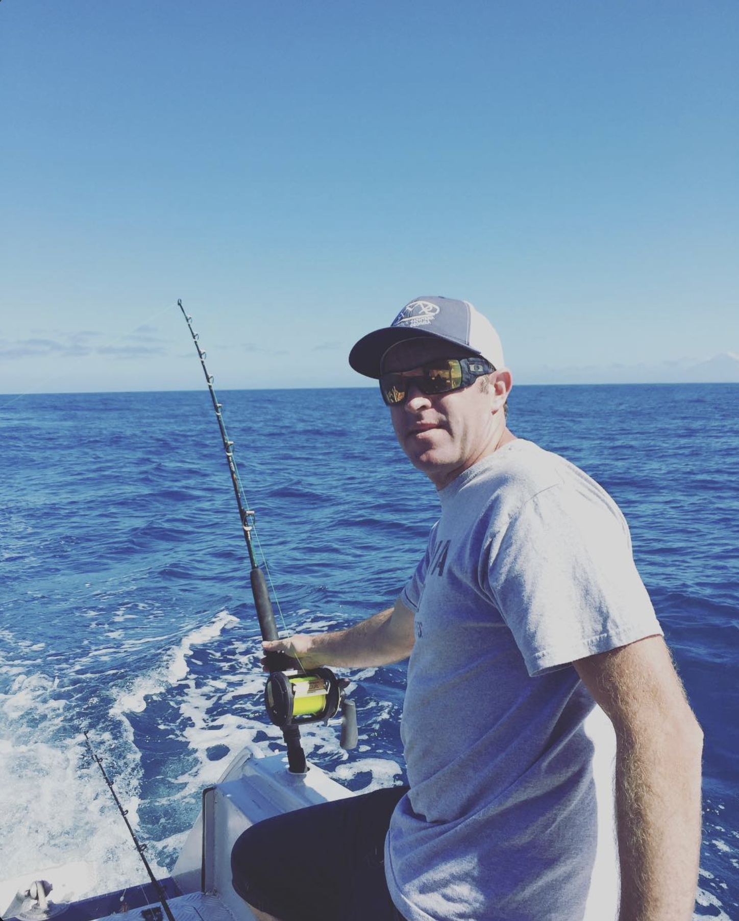 Man wearing a cap and sunglasses fishing from a boat in the open ocean