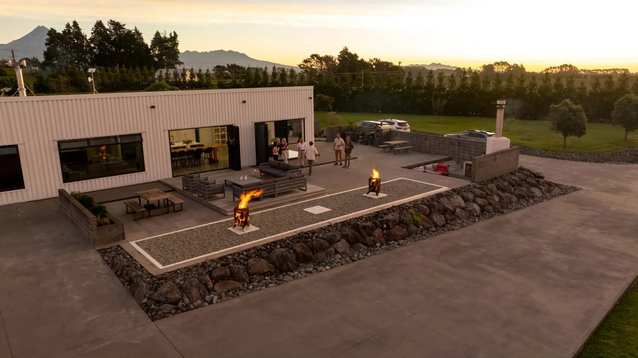 Modern outdoor patio with guests, fire pits, lounge seating, and mountain views at sunset