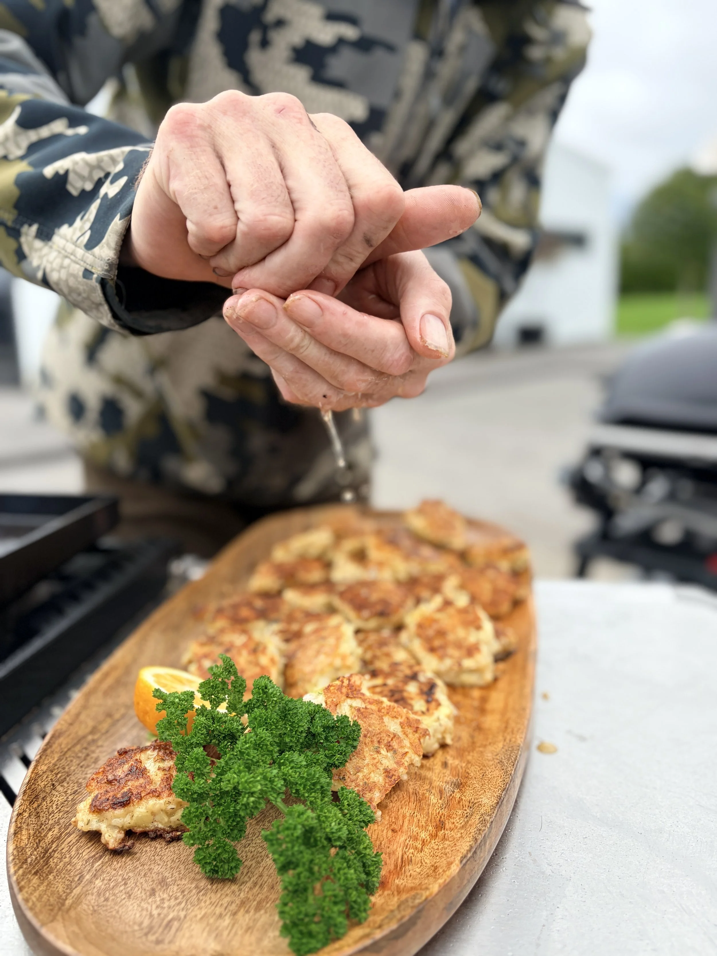 Chef holding a chicken cutlet over a wooden platter of grilled chicken, garnished with parsley and lemon