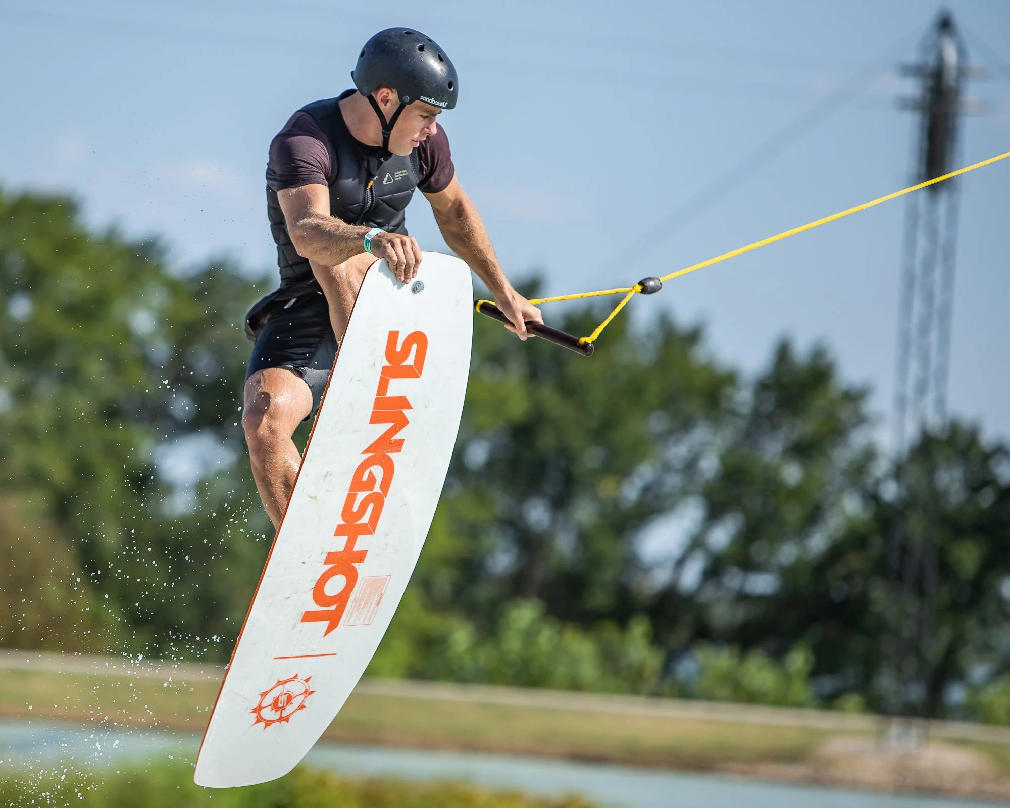 A man wakeboarding on water, holding a handle connected to a yellow tow rope, wearing a black helmet and life vest.