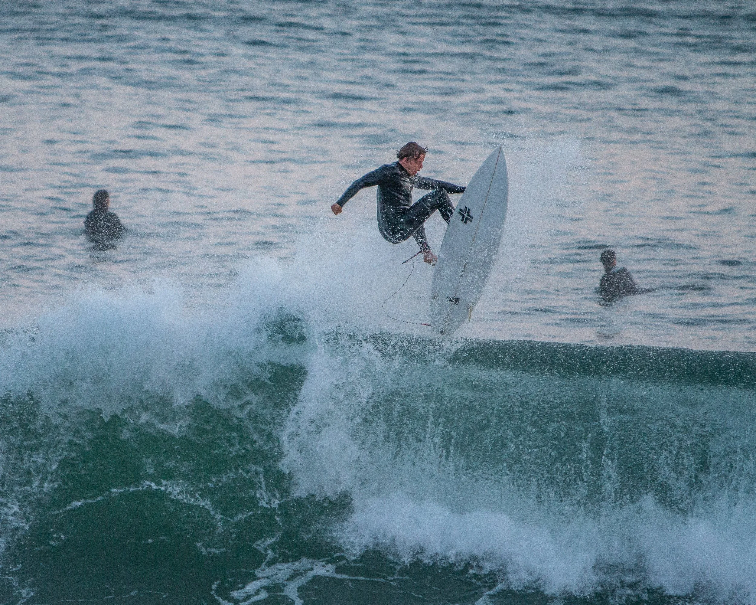 A person skateboarding on the ocean, with two people in the water nearby.
