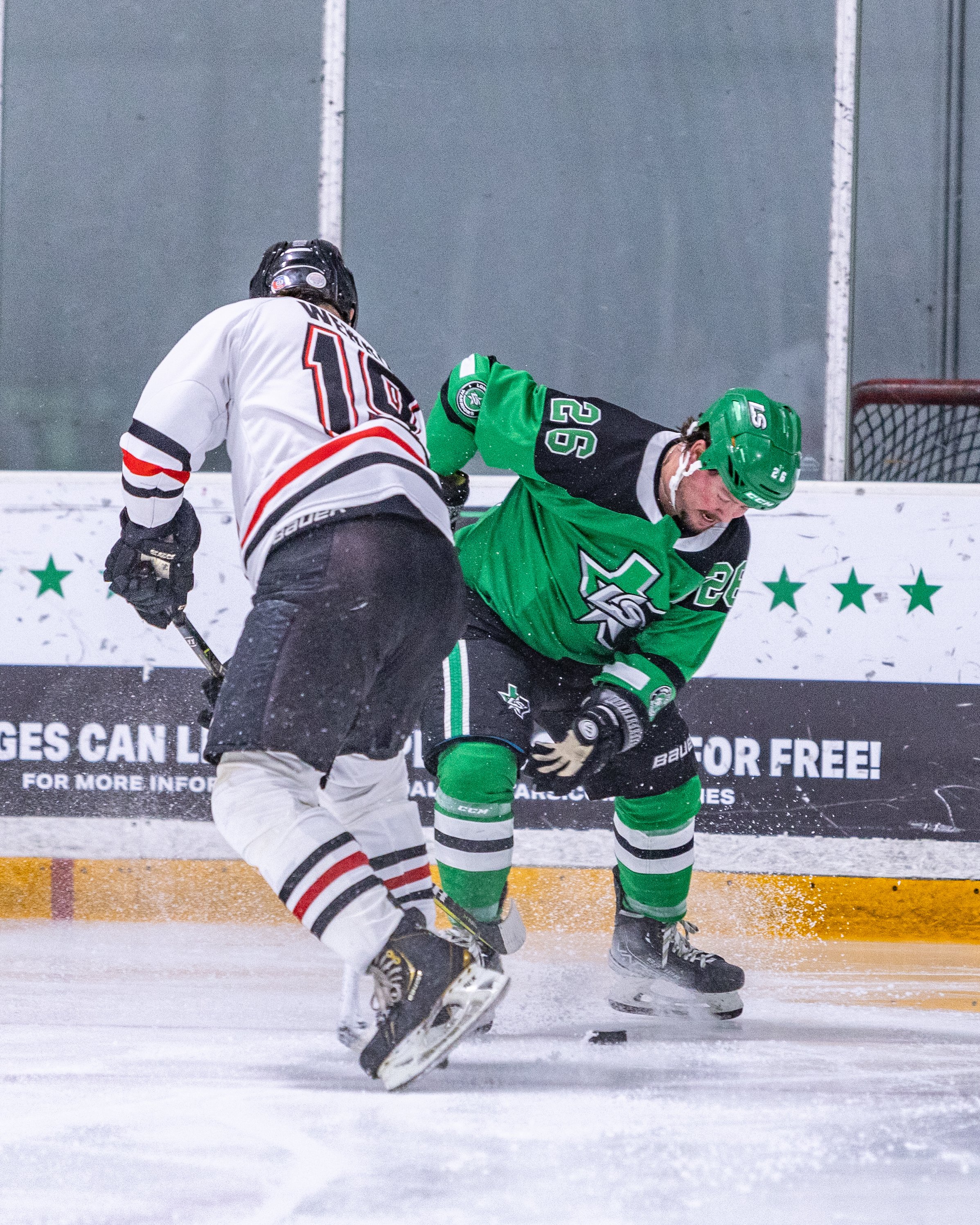 Two hockey players in a fight on the ice, one wearing a green jersey and the other a white jersey.