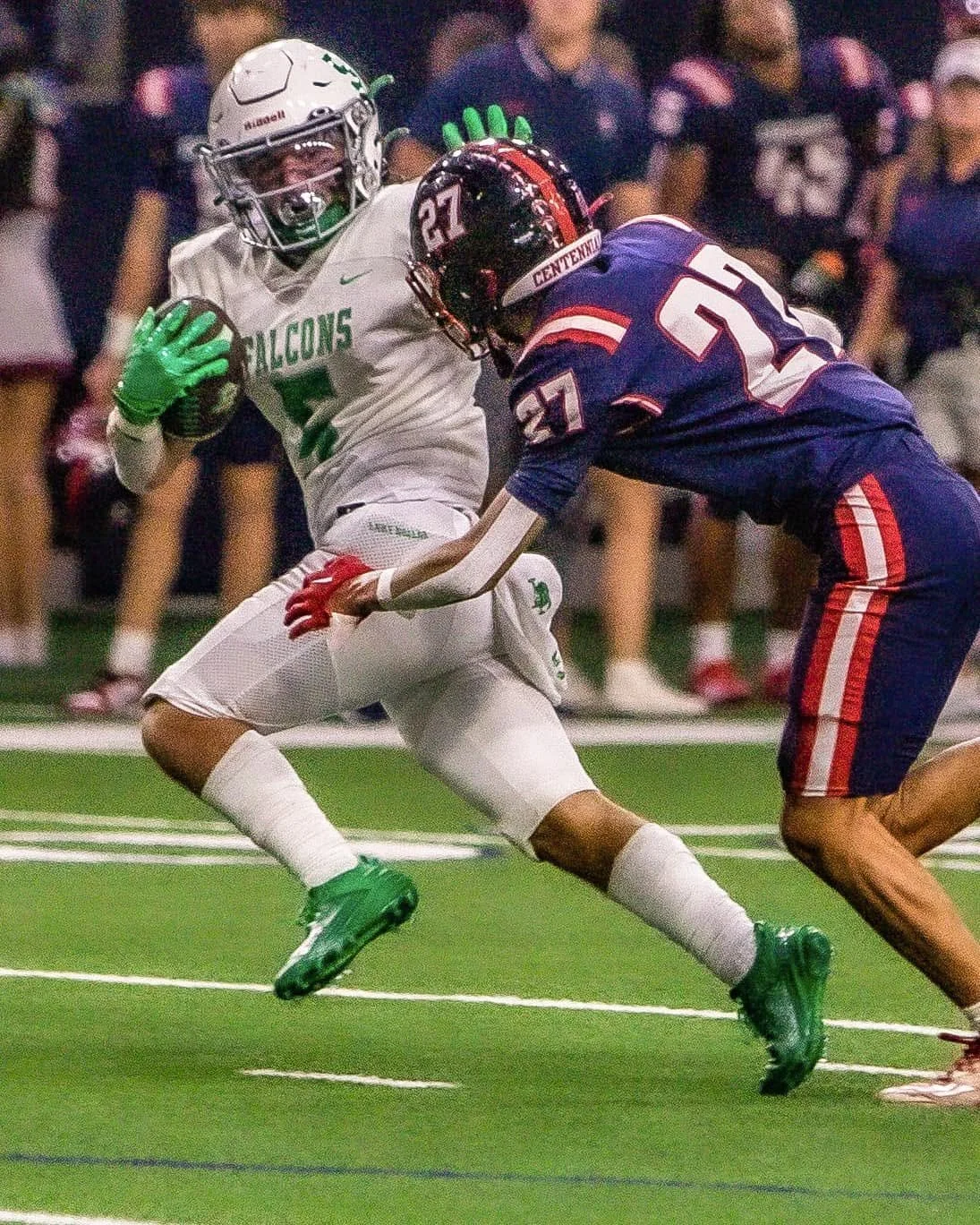 A football player from the Falcons team running with the ball while a player from the opposing team attempts to tackle him during a game.