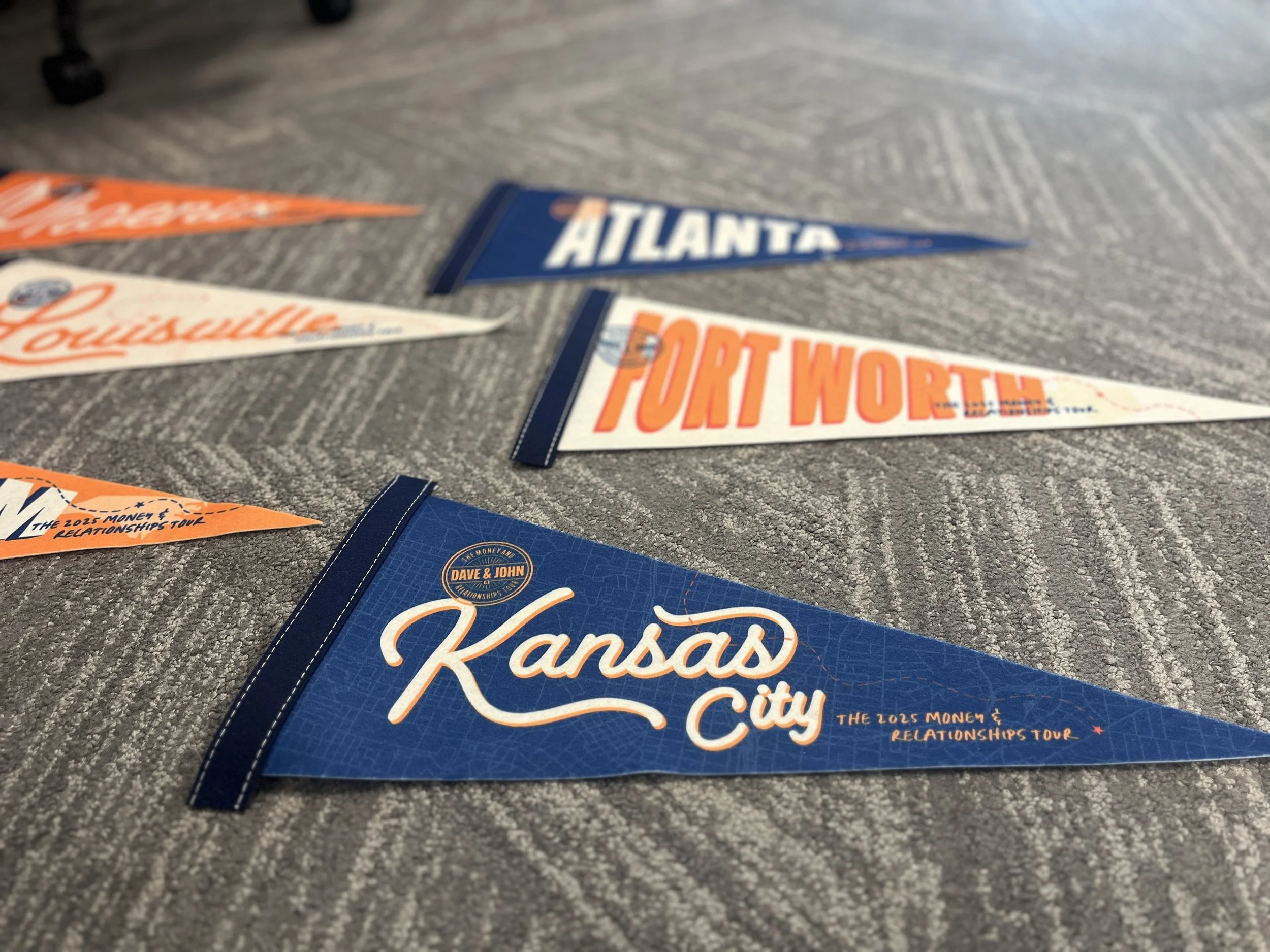 Close-up of souvenir pennants for Kansas City, Fort Worth, and Atlanta laid out on a gray carpeted floor.