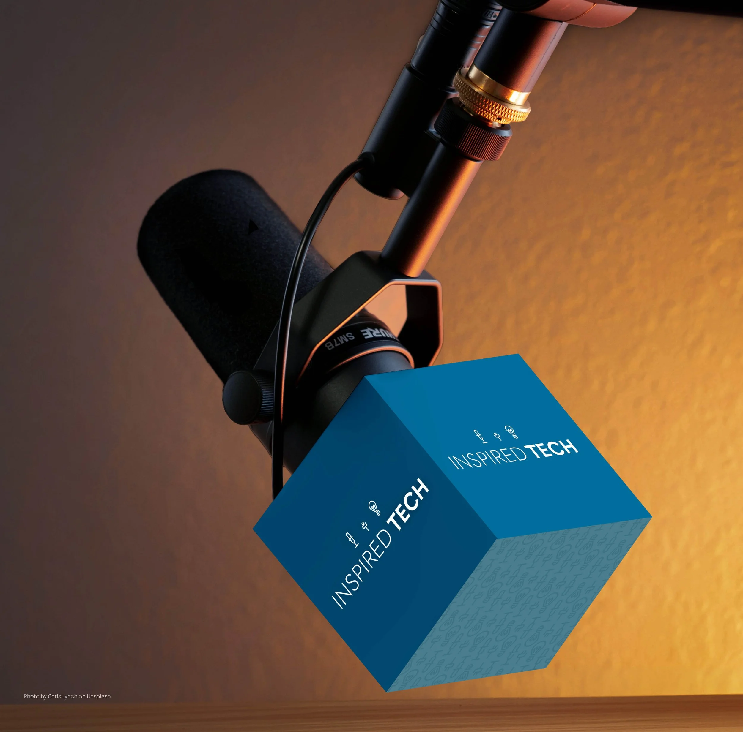 Close-up of a microphone and blue printed paper with the text 'Inspired Tech' on a wooden surface.