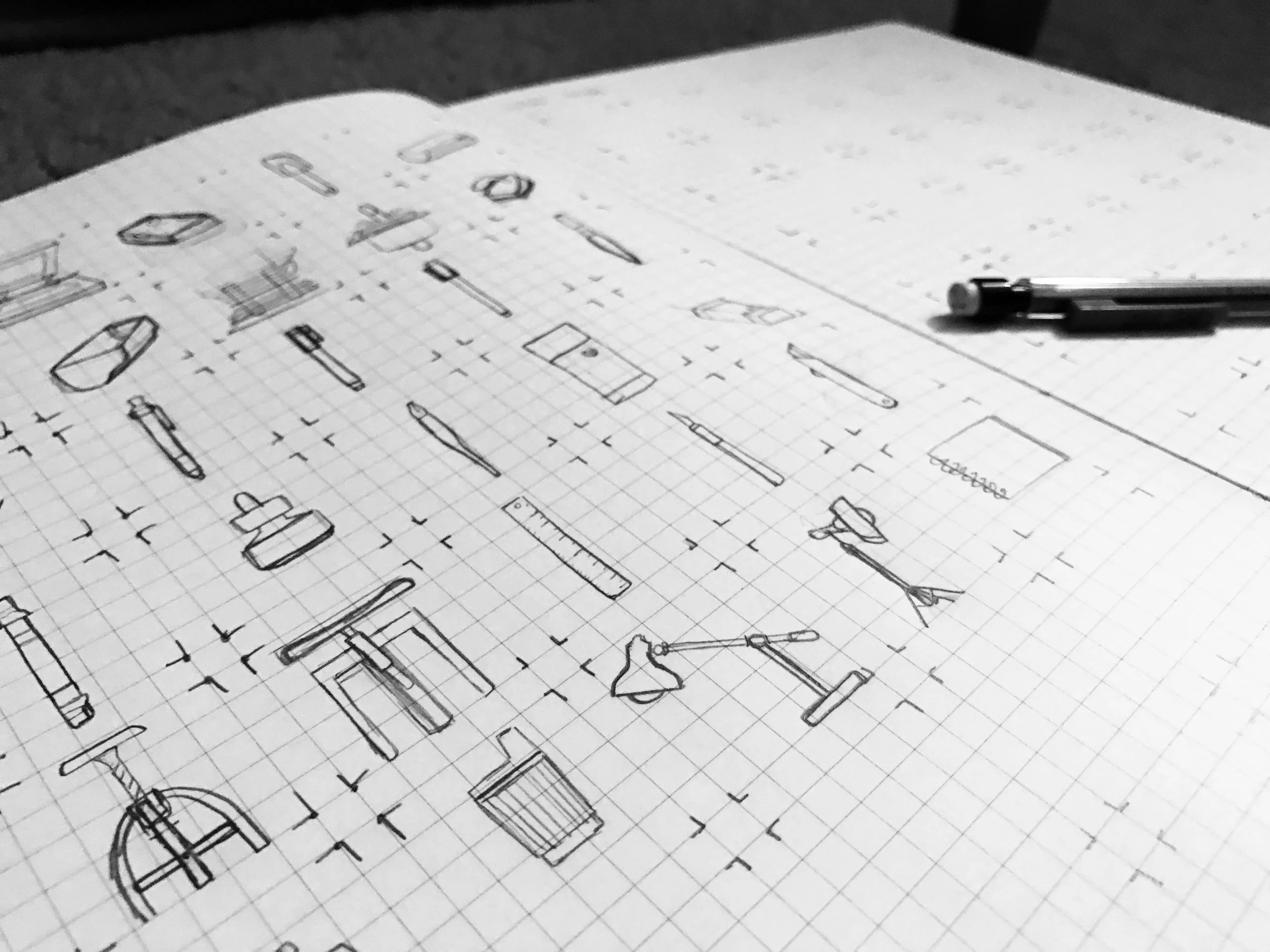 Black and white technical drawings and sketches of various studio items and art tools on graph paper, with a pencil resting on the paper.