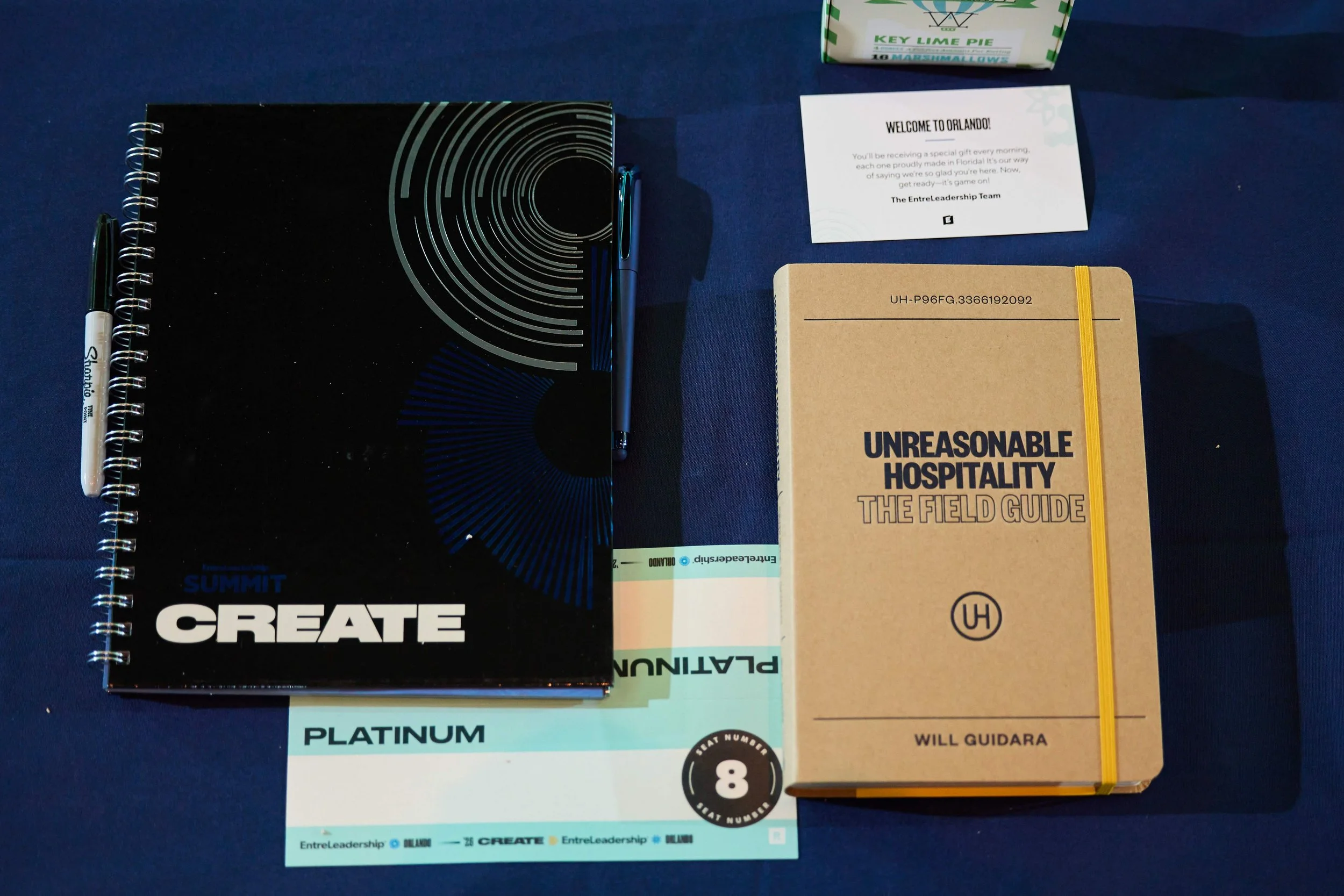 	
Gifts that Platinum tier attendees get at their seat. It includes the Summit Create workbook, a Platinum name tent, a welcome card, branded pen, Will Guidara's book, and a snack.