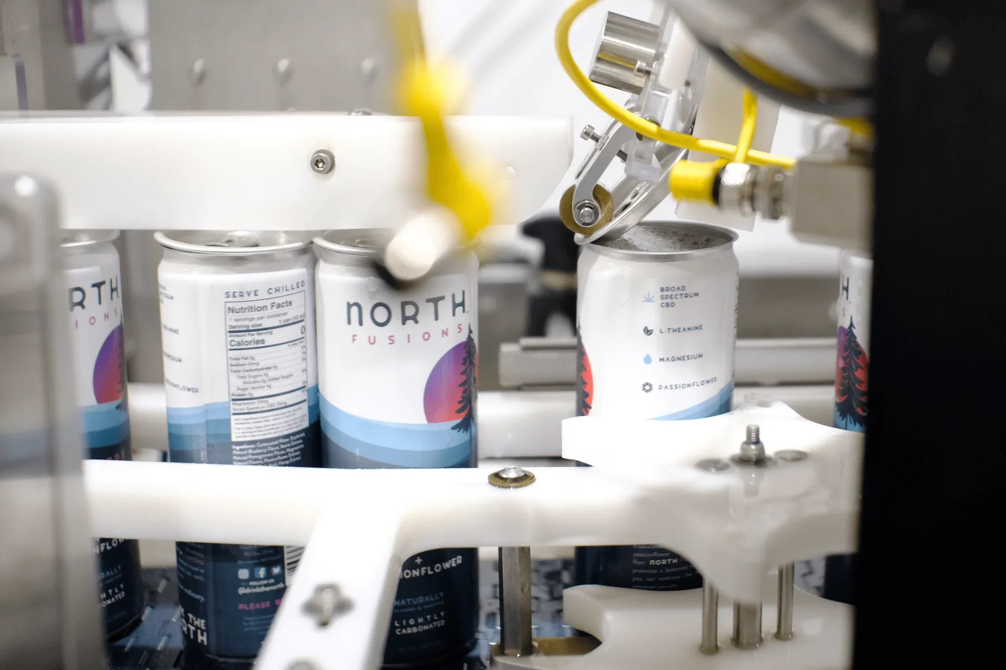 Close-up of a manufacturing line filling cans with a product, with a robotic arm handling the cans.