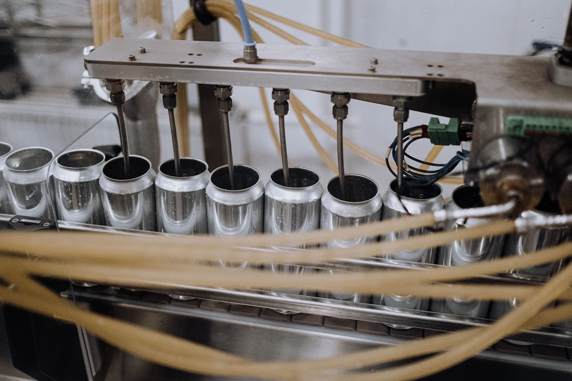 A mechanical conveyor system with metal cans moving along a track, propelled by metal rods and connected machinery. The system appears to be part of a factory or production line.