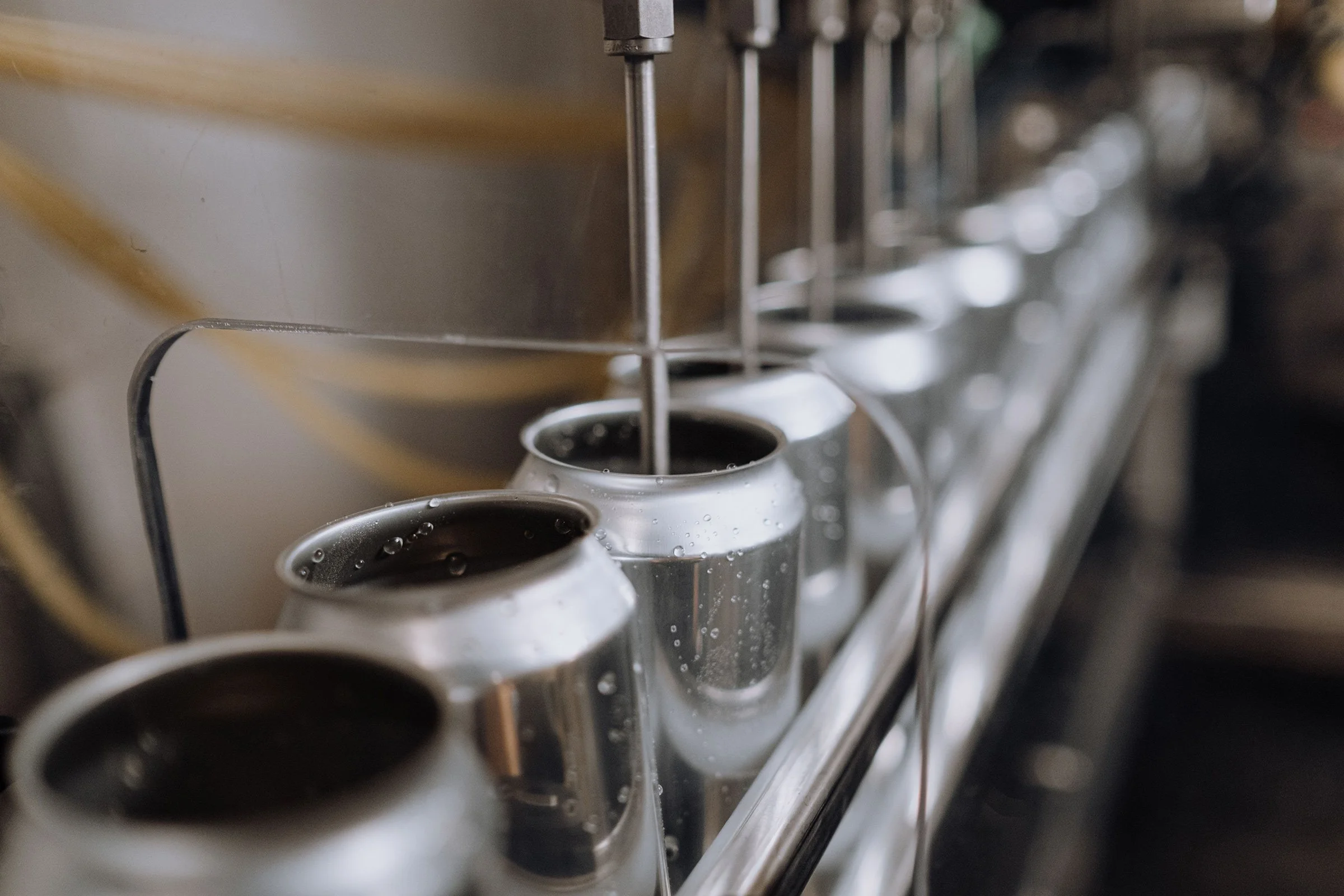 Close-up of beer cans in a vending machine with one can being filled with liquid from a spout.