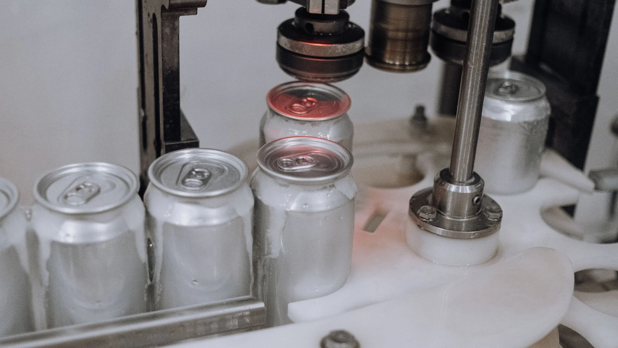 Close-up of a manufacturing process where aluminum cans are being stamped with a red laser or light, with some cans already filled and sealed.