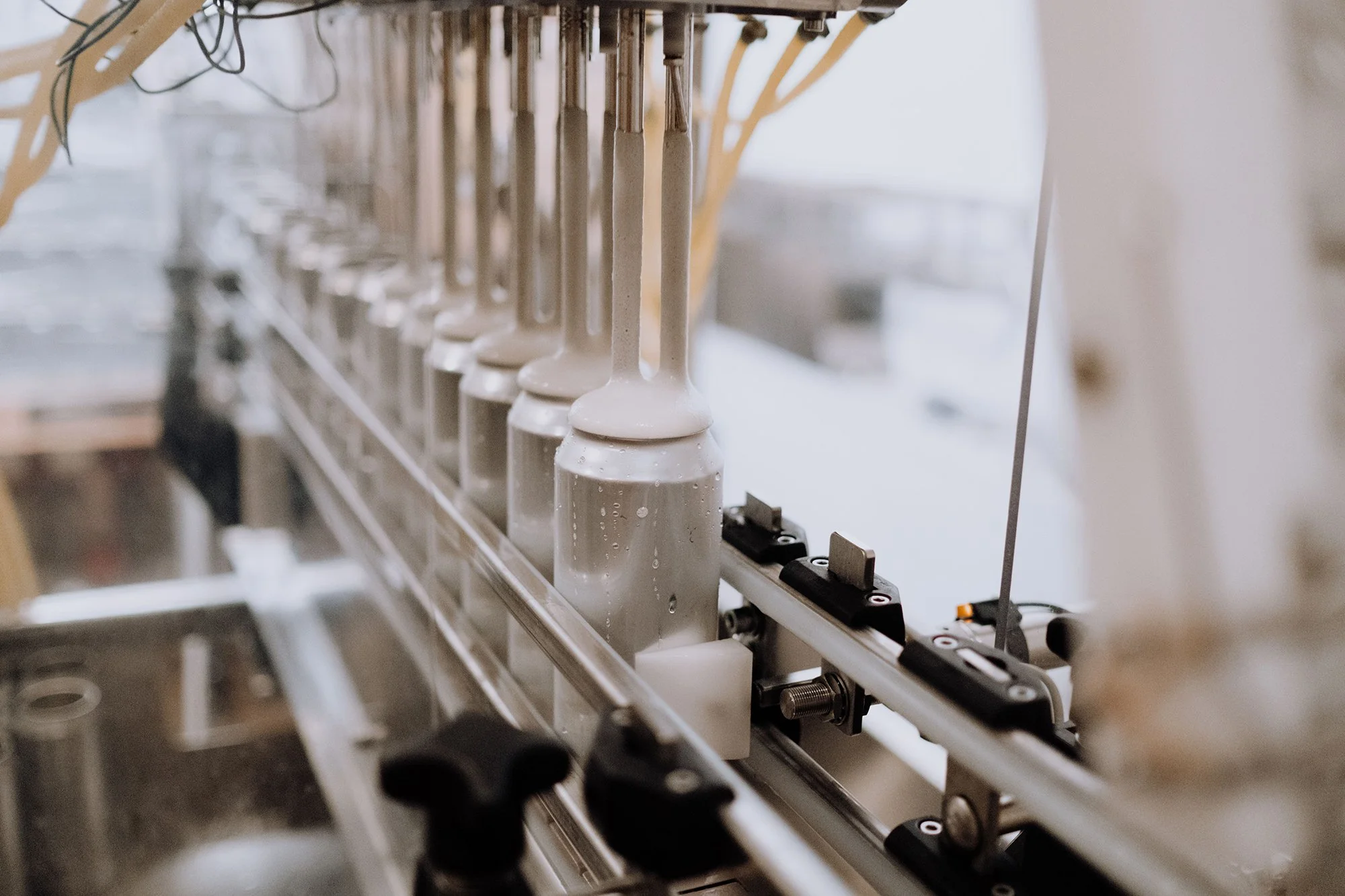 A row of glass bottles moving along a conveyor belt in a manufacturing or filling process, with some water droplets on the bottles.