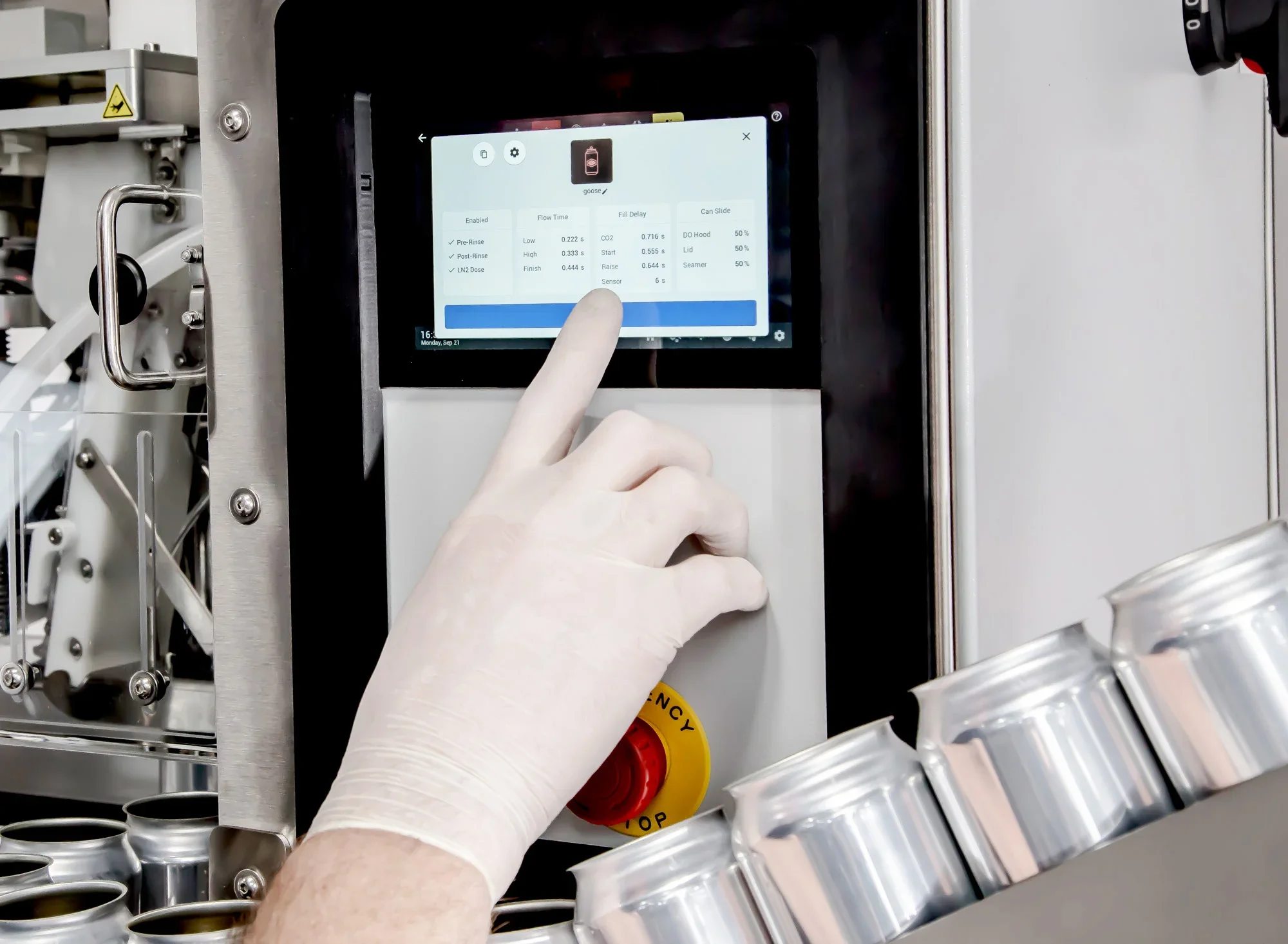 Close-up of touchscreen panel displaying settings for a machine, with a gloved hand pointing at the screen. The background shows part of the machine's metallic and plastic components.