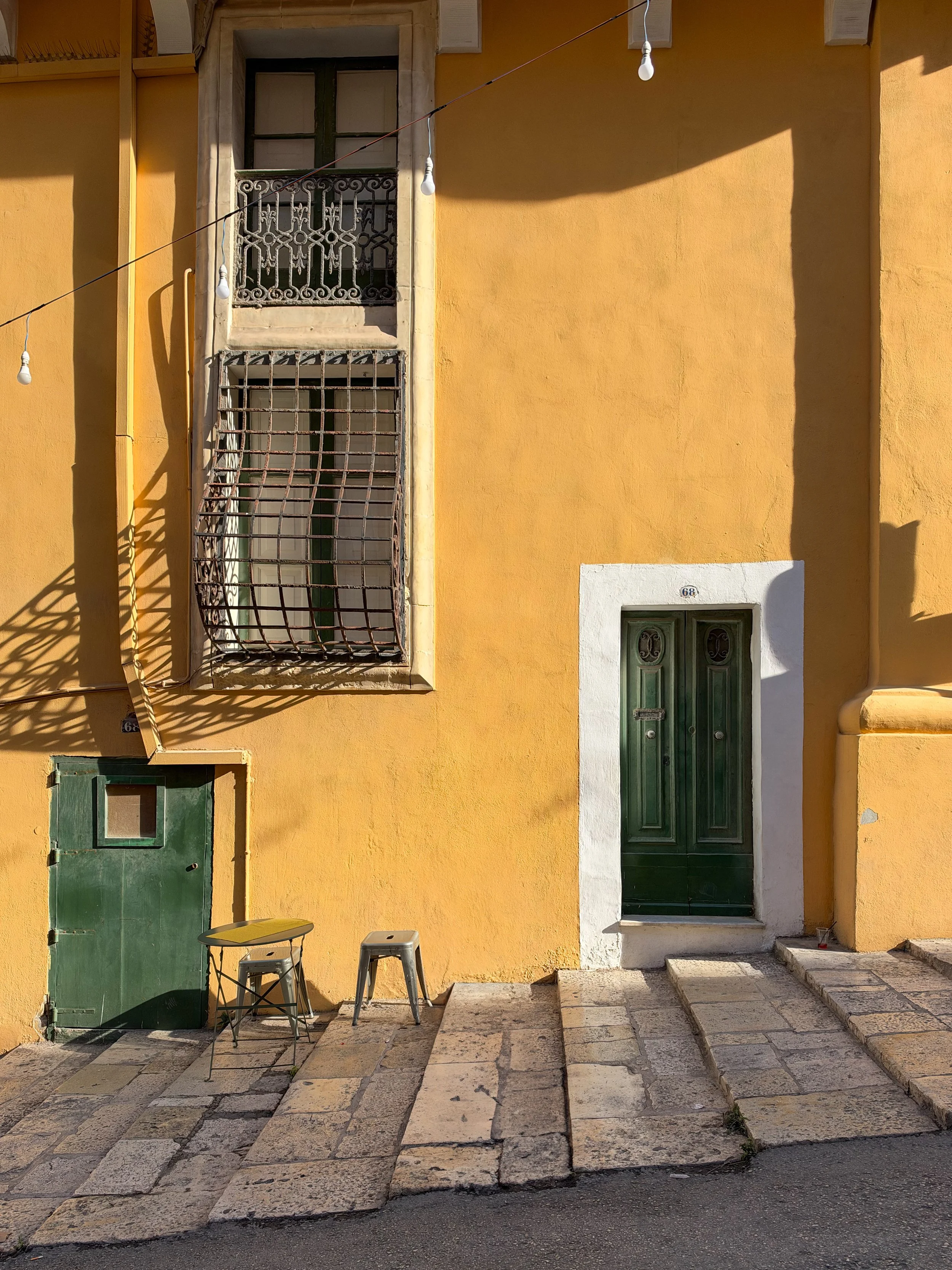 Yellow building with green door and windows, two chairs, and stone steps leading to the entrance.