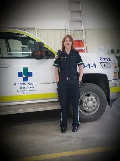 A female emergency medical services worker standing in front of an ambulance at an indoor facility.