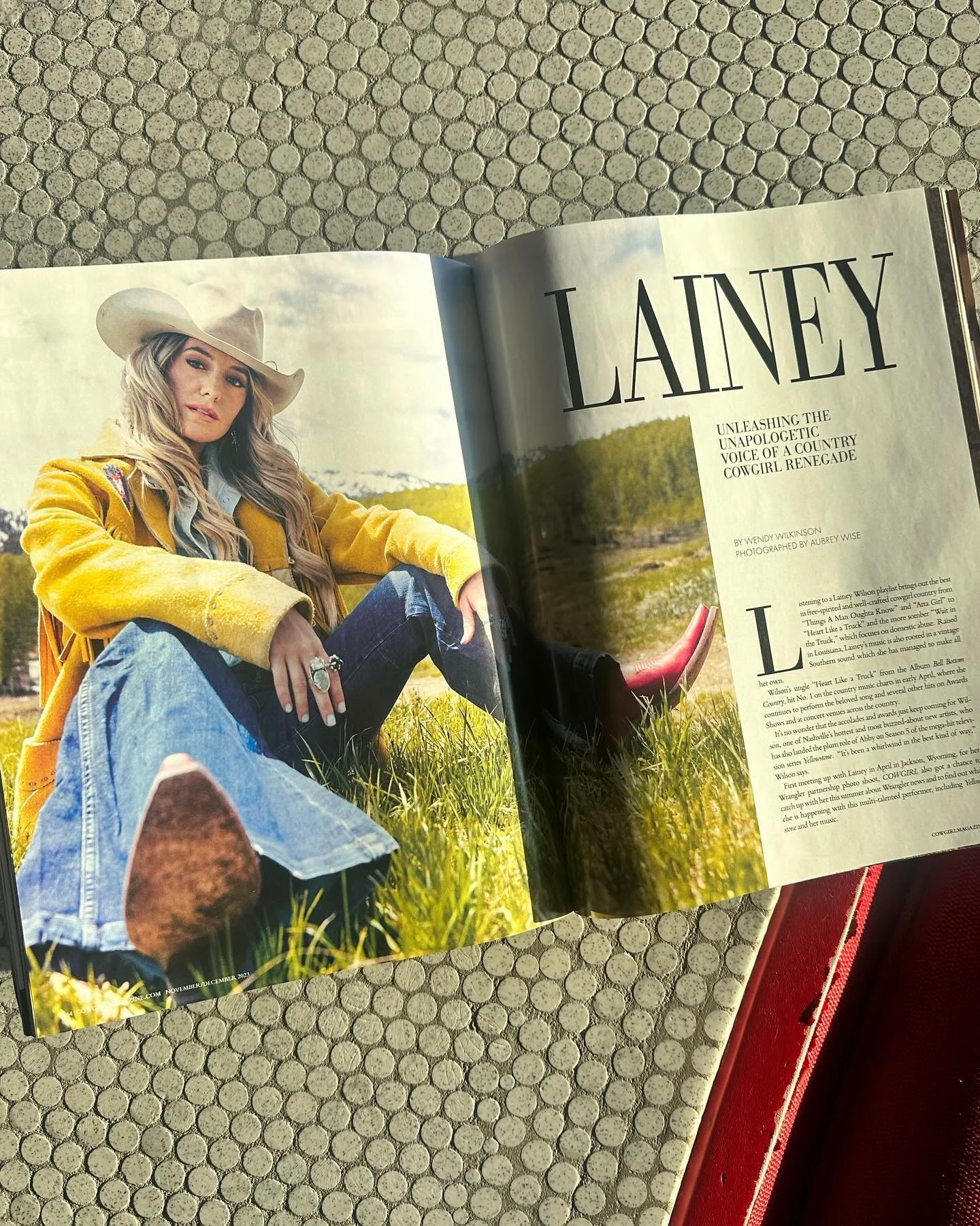 Open magazine featuring a woman in a yellow jacket and cowboy hat sitting outdoors in a grassy field with trees in the background.