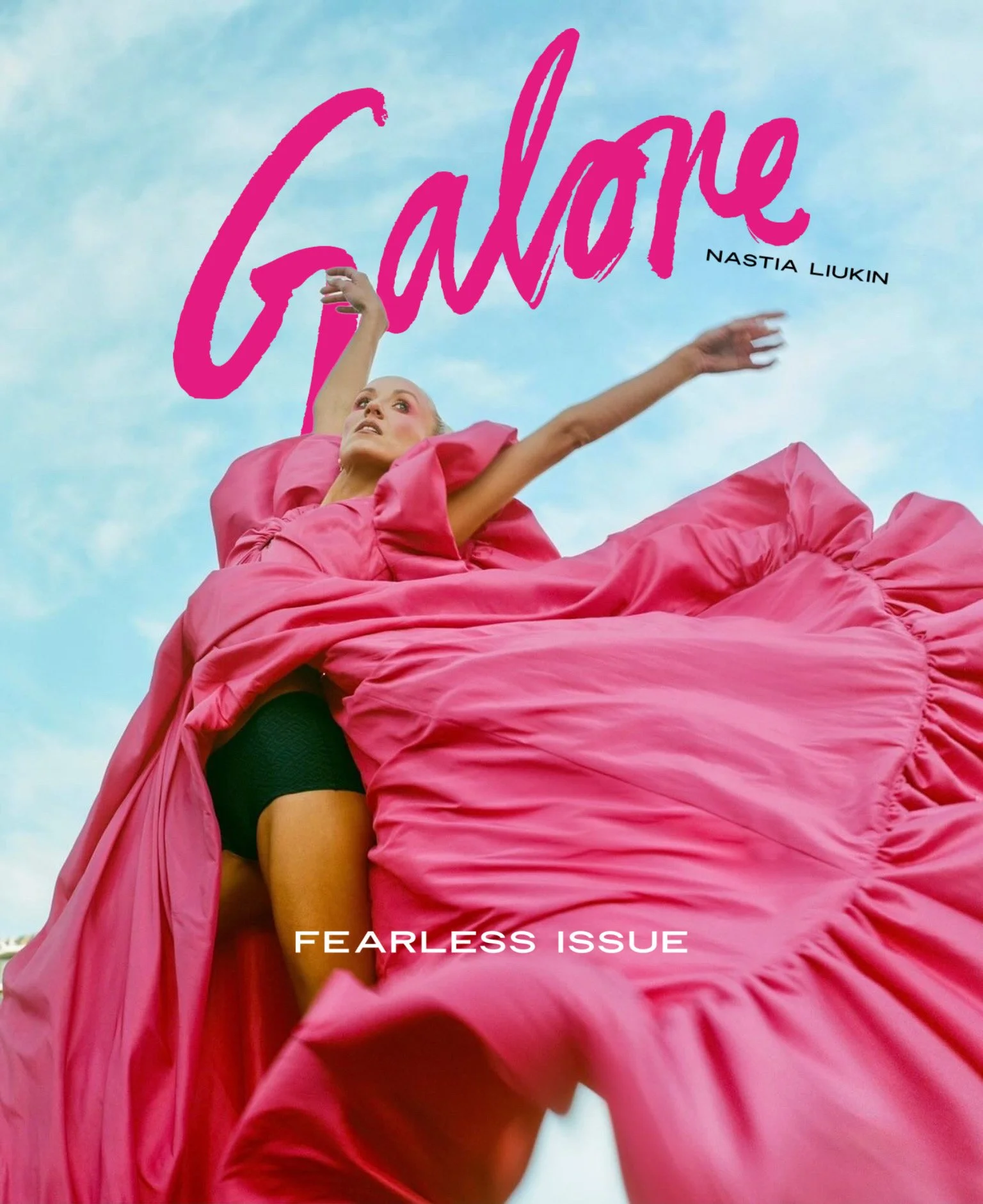 A person in a pink dress lying on the ground, reaching upward against a blue sky background. The text on the image says 'Fearless Issue' and 'Galaore' in pink and black font.