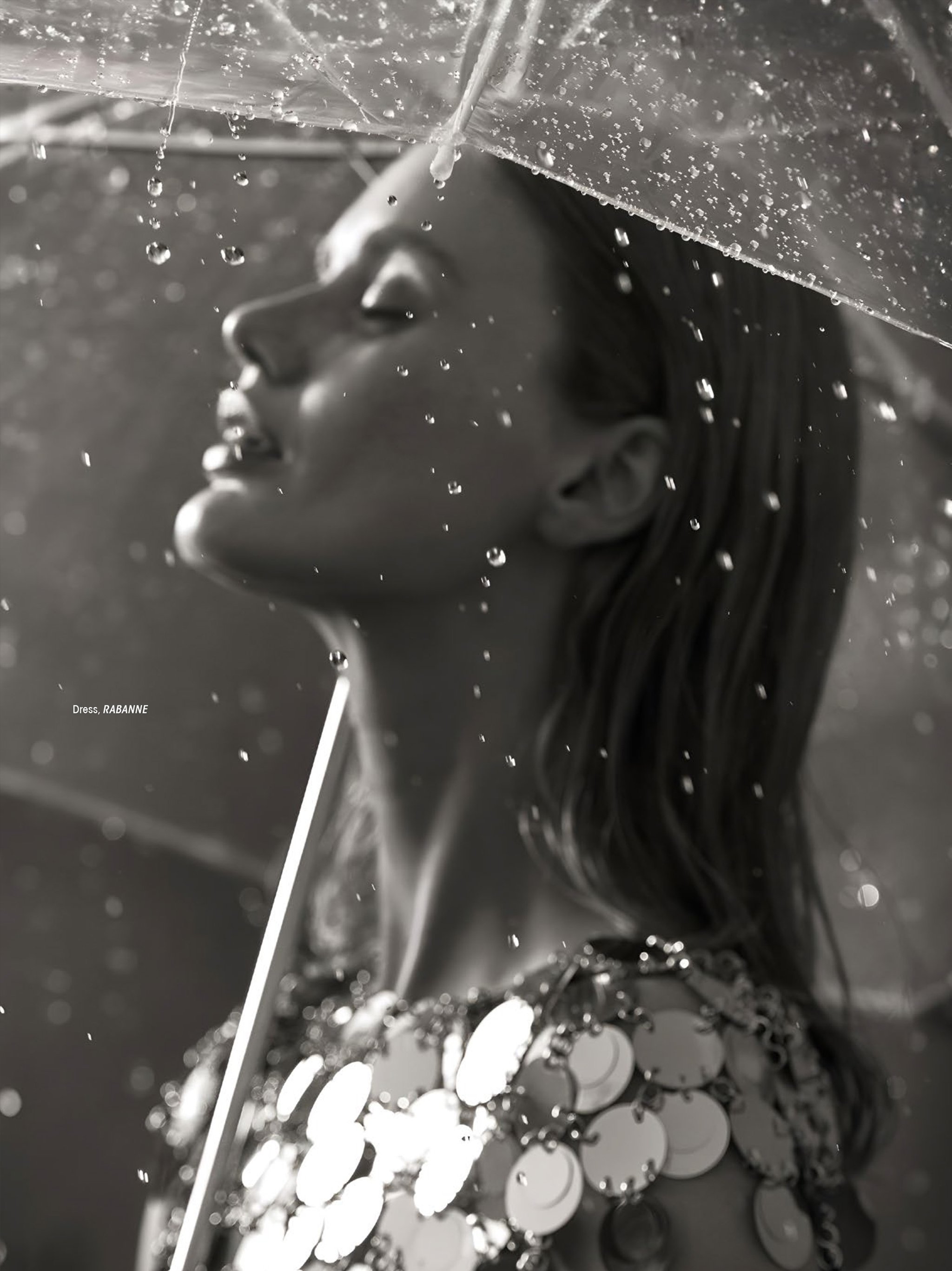 Black and white photo of a woman lying down with water droplets falling over her face. The woman has long, dark hair and closed eyes. The image gives a serene, calm, and artistic vibe.