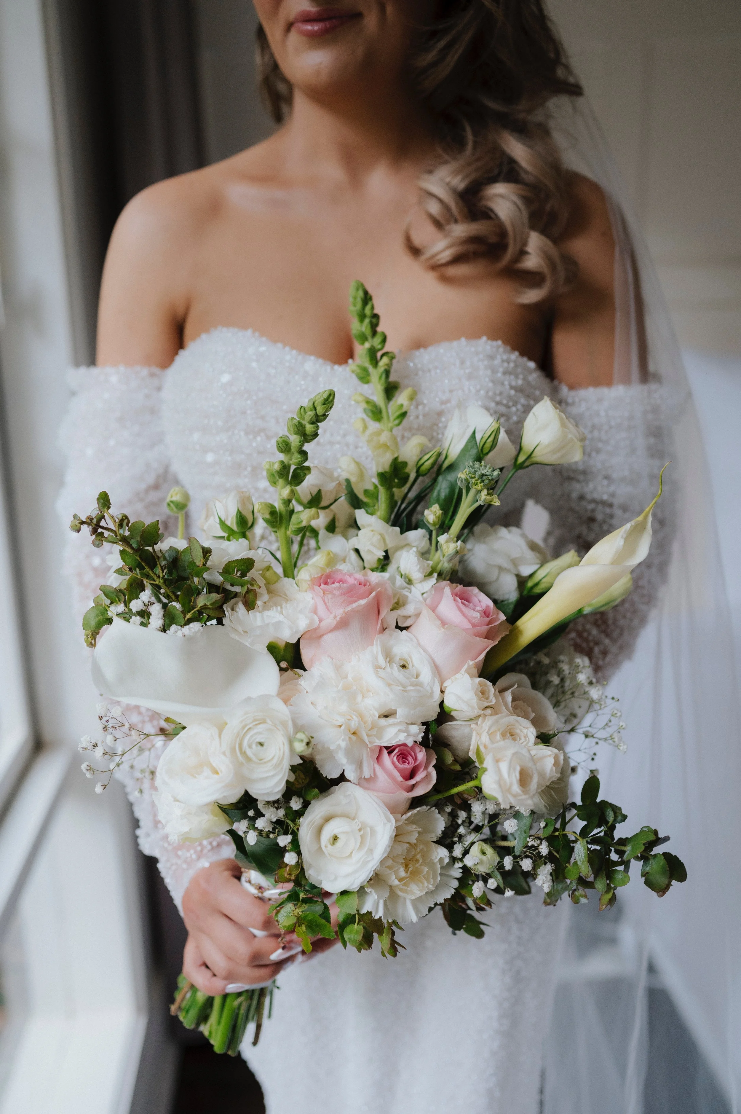 A woman in a wedding dress holding a large bouquet of white and pink flowers, with her face partially visible.