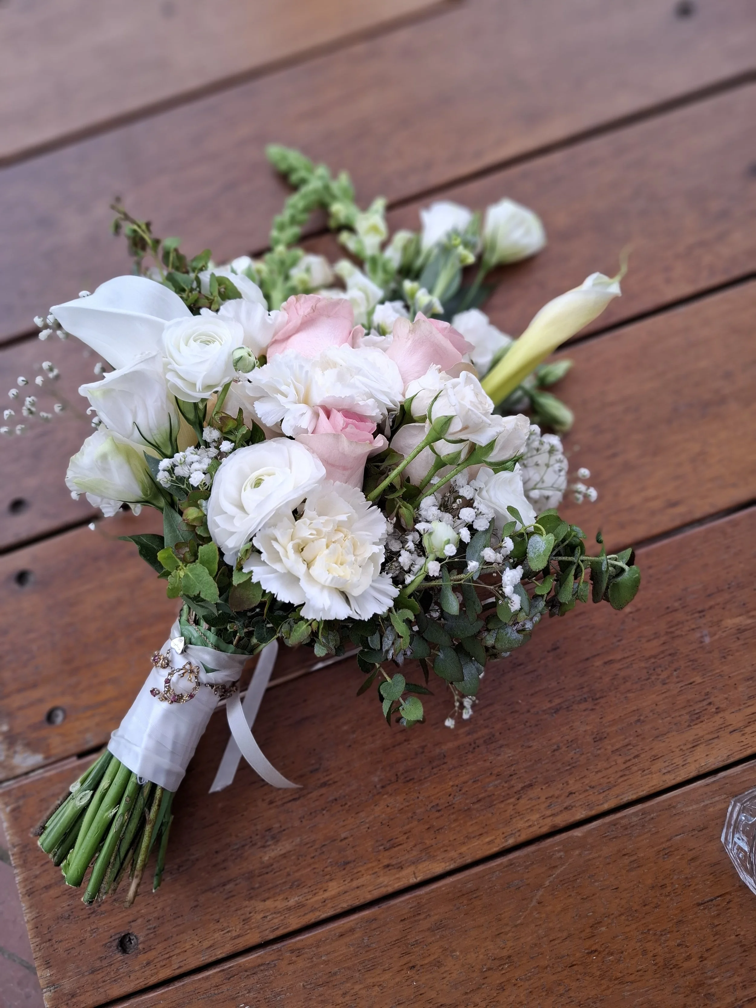 A bouquet of white and pink flowers with green foliage on a wooden surface.