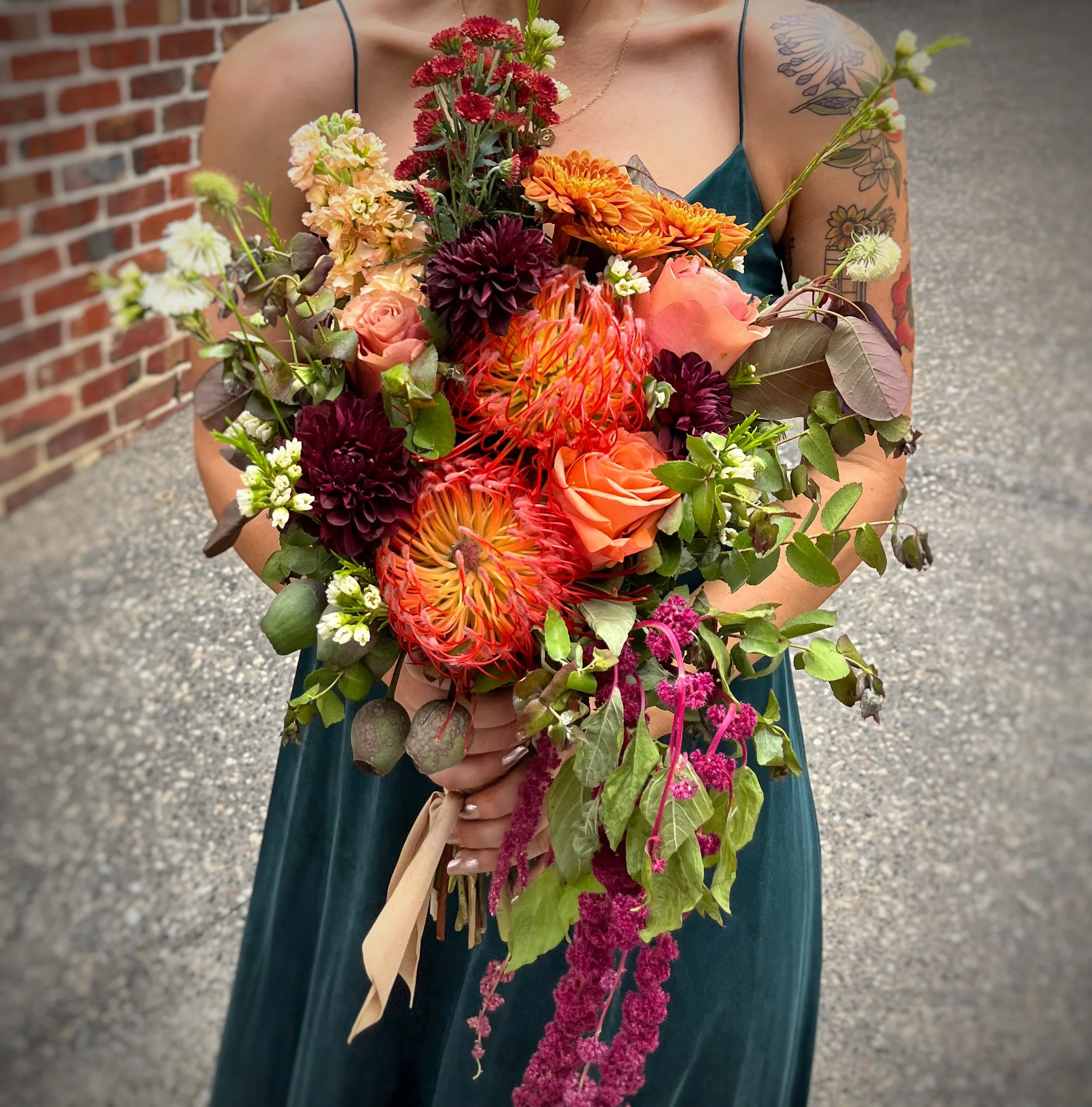 A person holding a large, colorful bouquet of flowers, with a brick wall background.