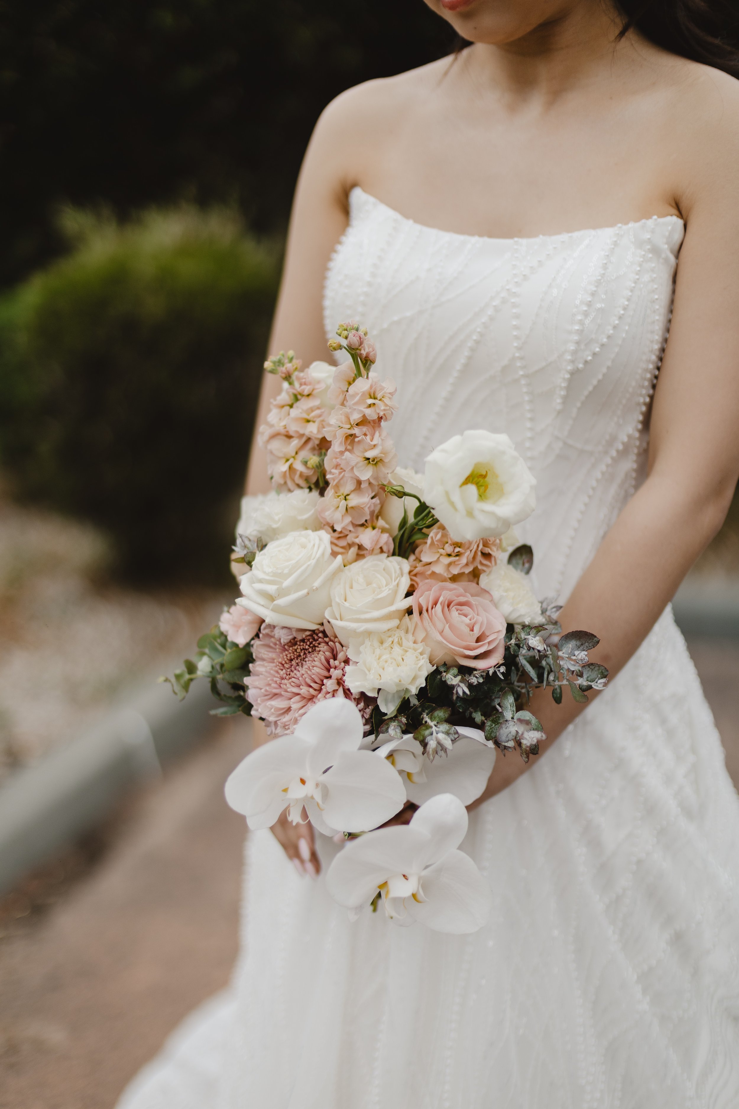 A woman in a strapless wedding dress holding a bouquet of pink, white, and cream flowers, including roses and orchids.