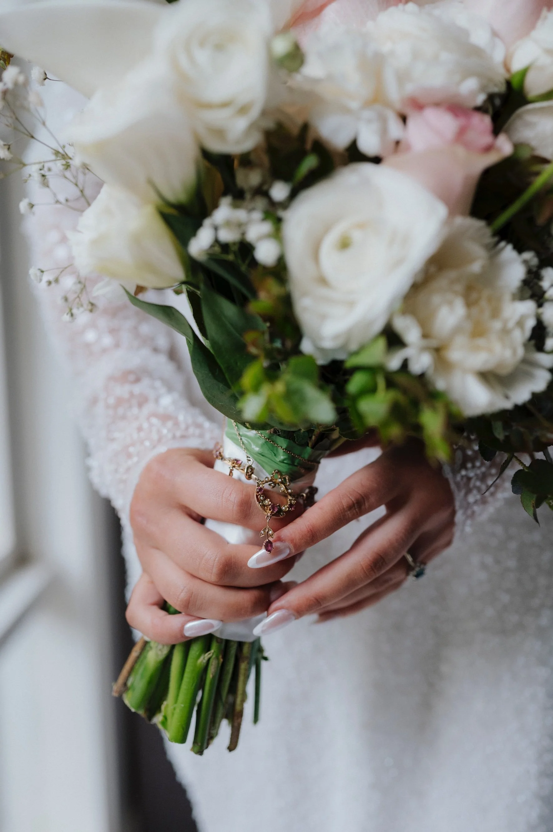 Person holding a bouquet of white roses, pink roses, baby's breath, and greenery, with rings and jewelry on their fingers and wrist.