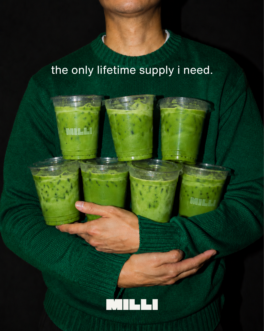 Person in a green sweater holding seven Milli iced matcha drinks. Text: the only lifetime supply i need.