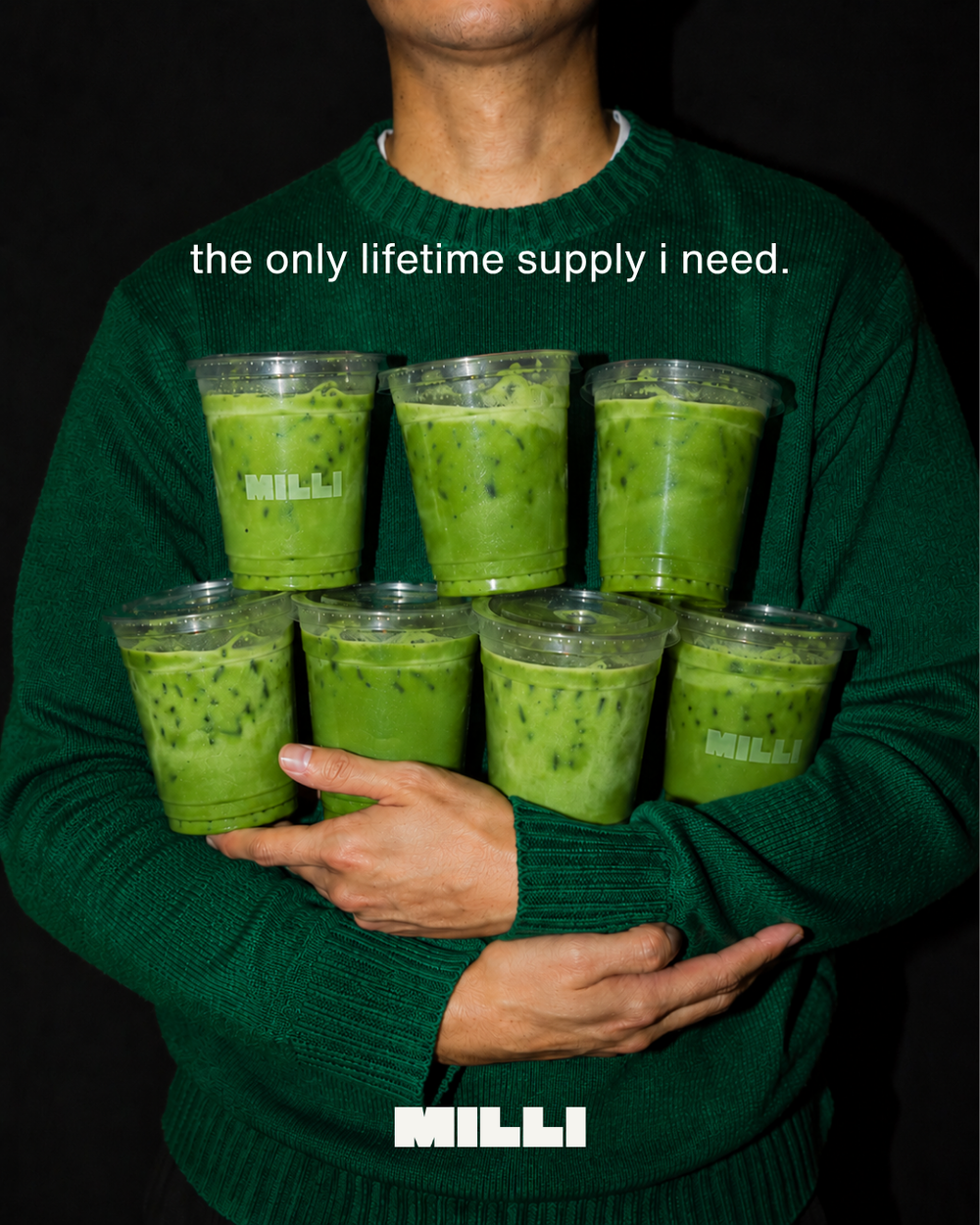 Person in a green sweater holding seven Milli iced matcha drinks. Text: the only lifetime supply i need.