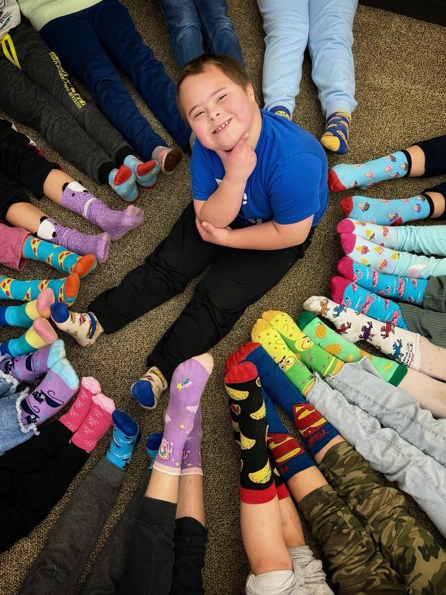 A boy in a blue shirt smiling in the middle of a circle of children in colorful socks