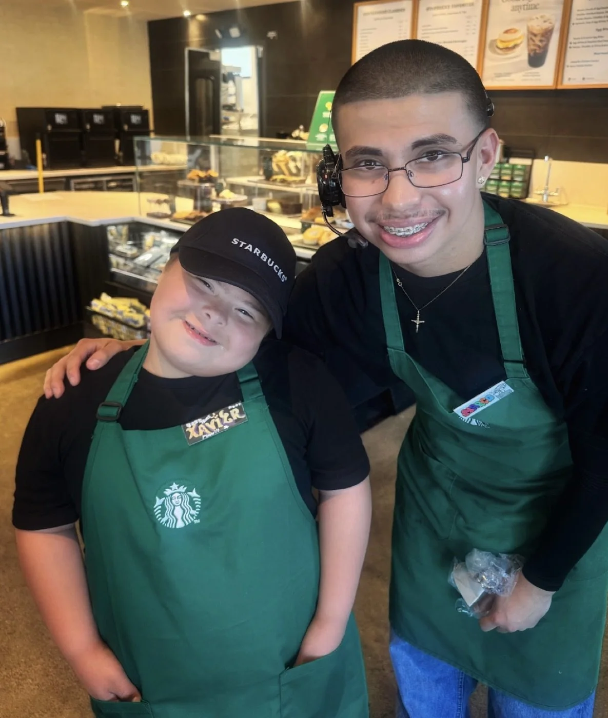 Xavier smiling beside a teammate in green aprons