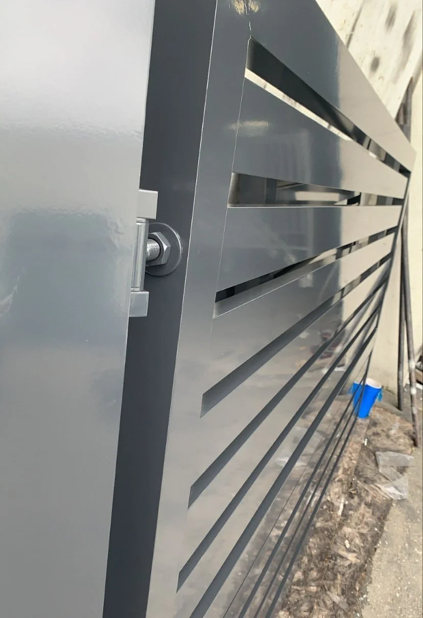 Close-up of a metallic gray structure, possibly a fence or gate, with horizontal slats and a bolt fastening it to a vertical post, on a construction site or outdoors.