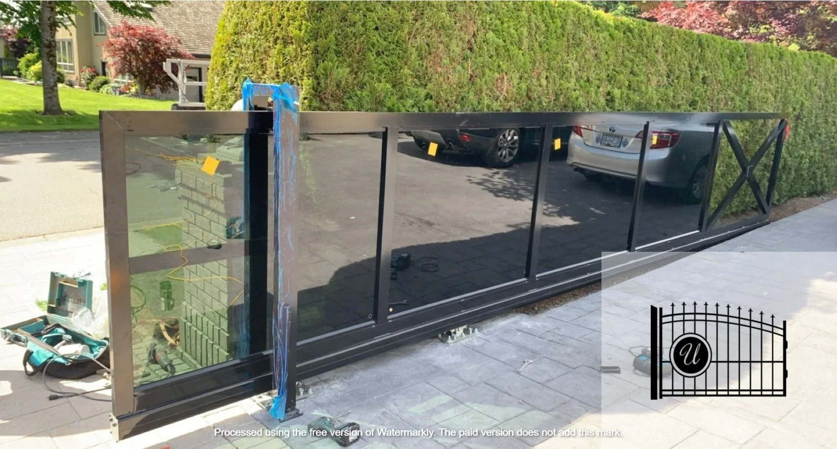 A black metal and glass fence panel under construction outside in a residential area, with tools and equipment nearby.