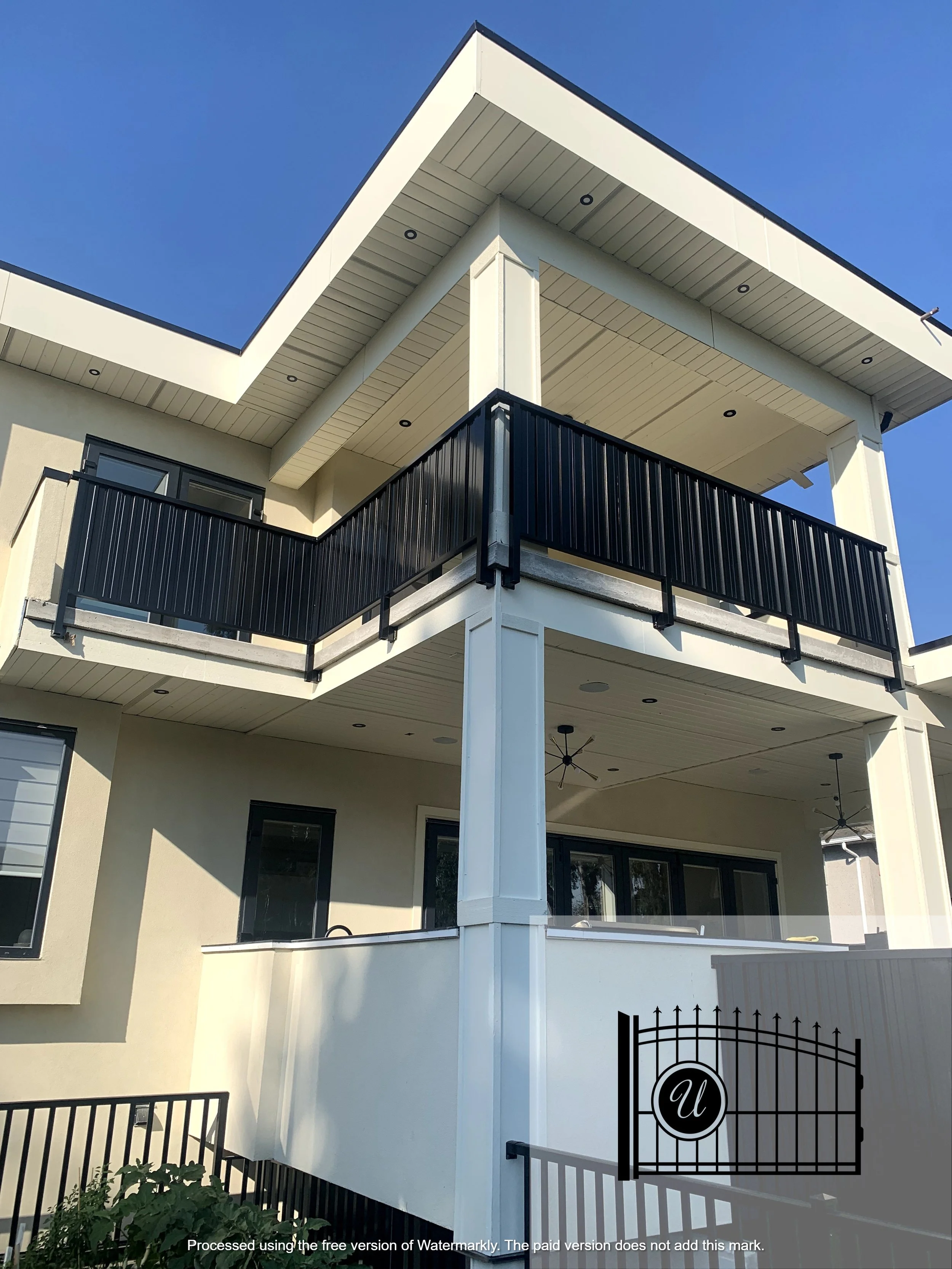 A modern, multi-level house with beige walls, black railings, and a balcony, under a blue sky.