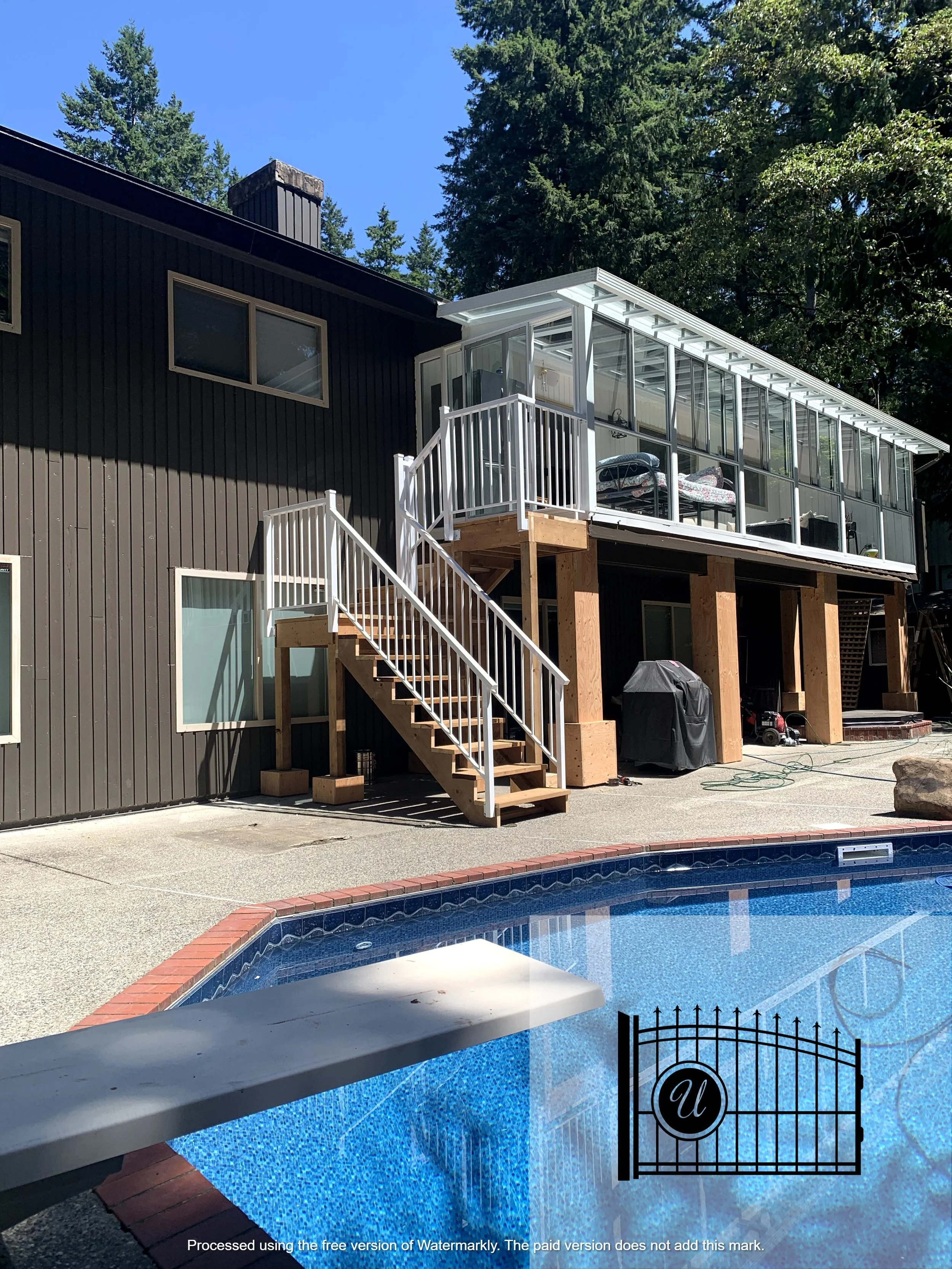 Residential house with a screened-in porch under construction, wooden steps leading up to the porch, and a swimming pool in the foreground with a black gate at the pool's edge.