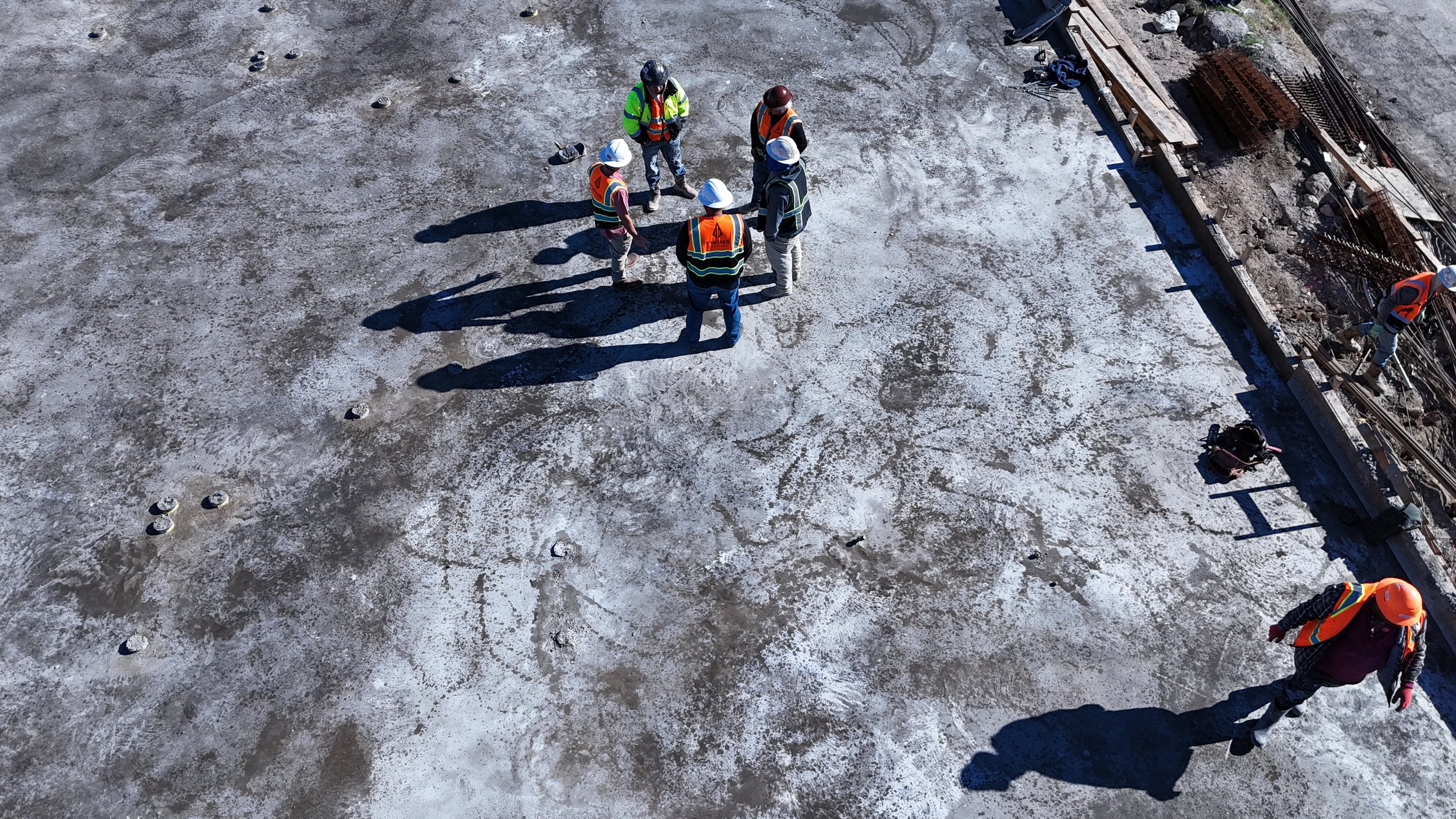 Overhead view of a construction crew in hardhats and reflective vests meeting on a work site.