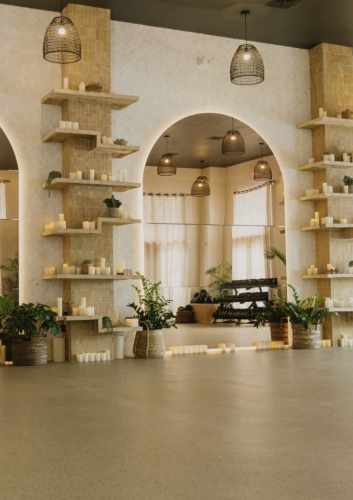 Studio interior with arched mirrors, wooden display shelves, pendant lights, and potted plants.