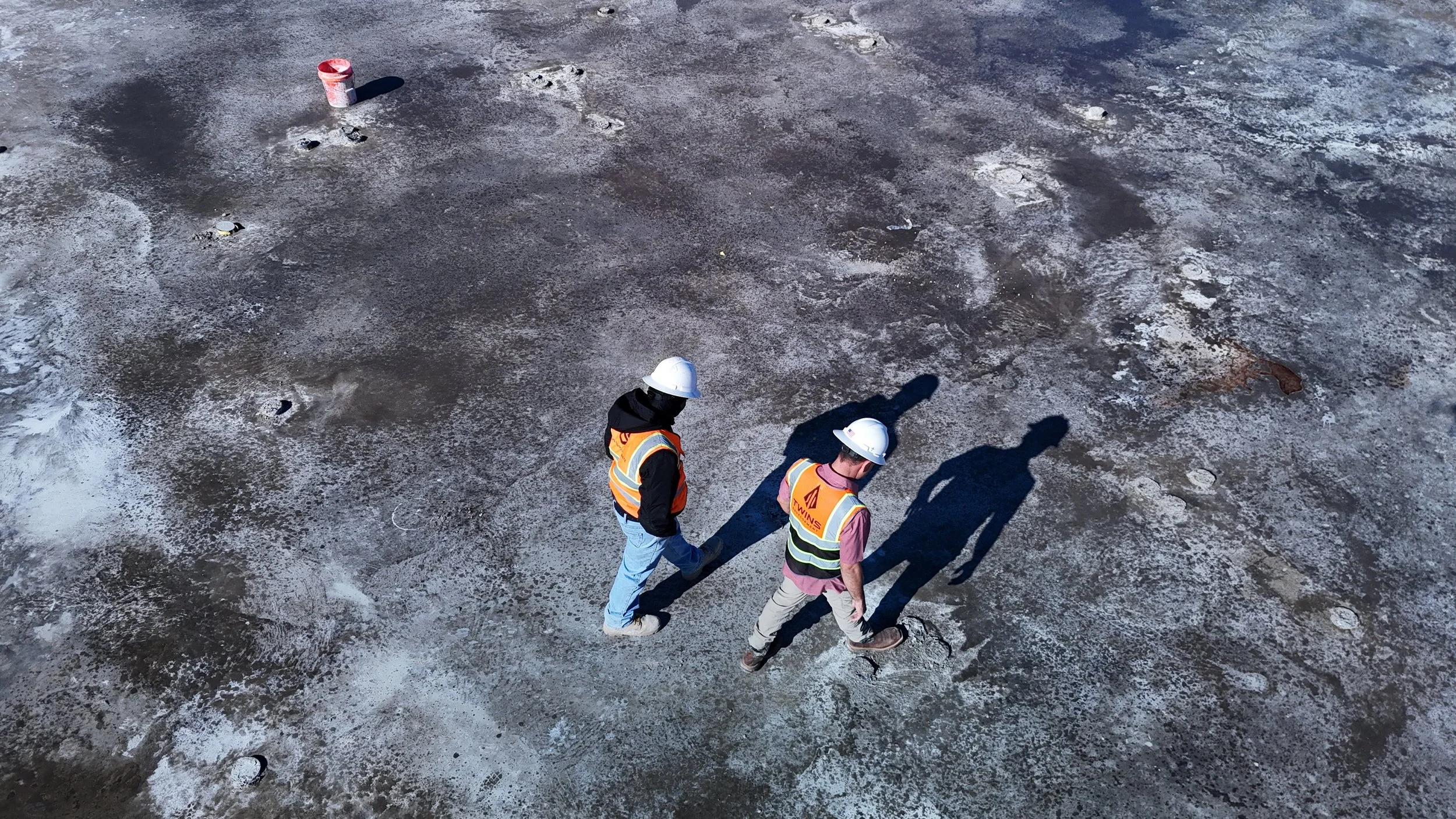 Two workers wearing hard hats on a concrete construction deck.