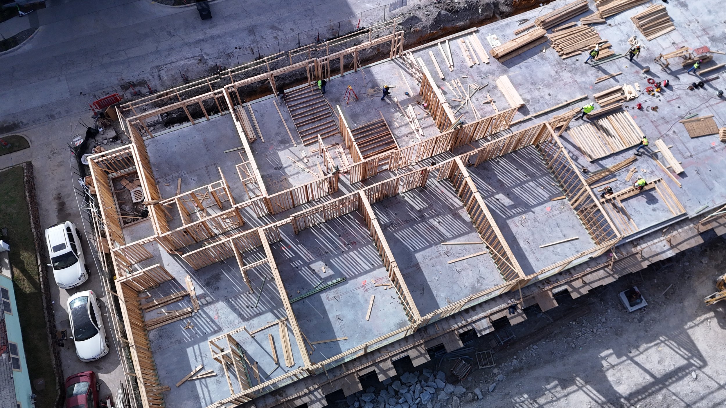 Aerial view of wood wall framing arranged across a concrete deck during building construction.
