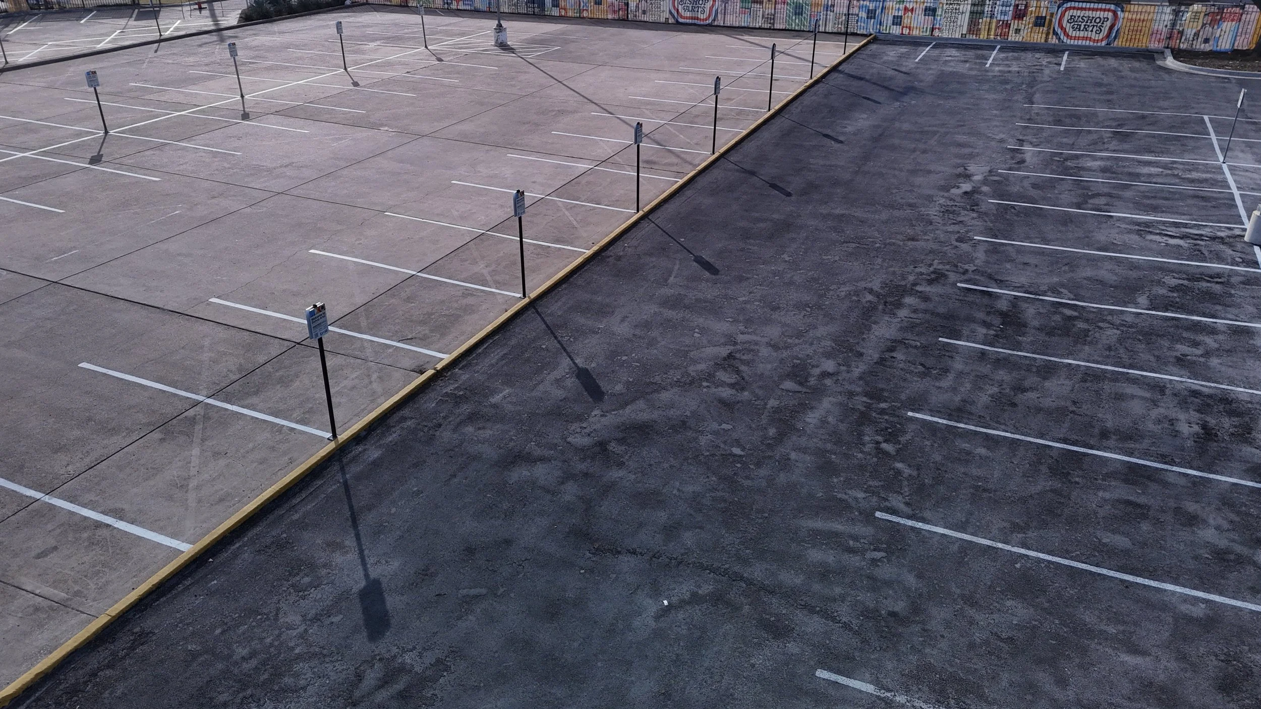 Aerial view of a striped parking lot with a yellow curb separating two paved areas.