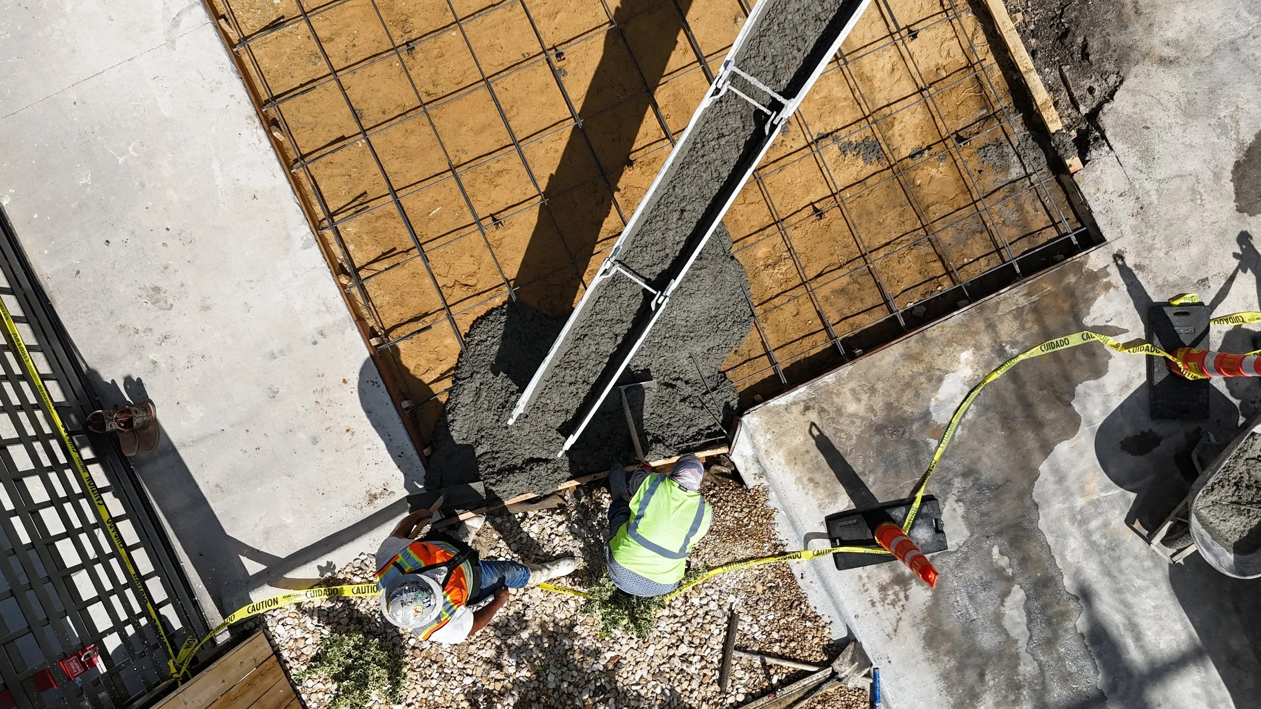 Overhead view of concrete placement beside a steel reinforcement grid.
