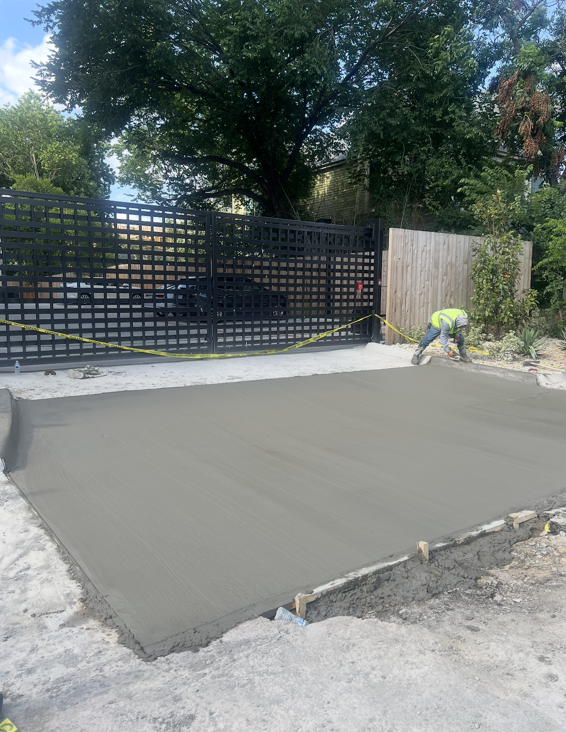 Freshly placed concrete sidewalk beside a black metal gate.